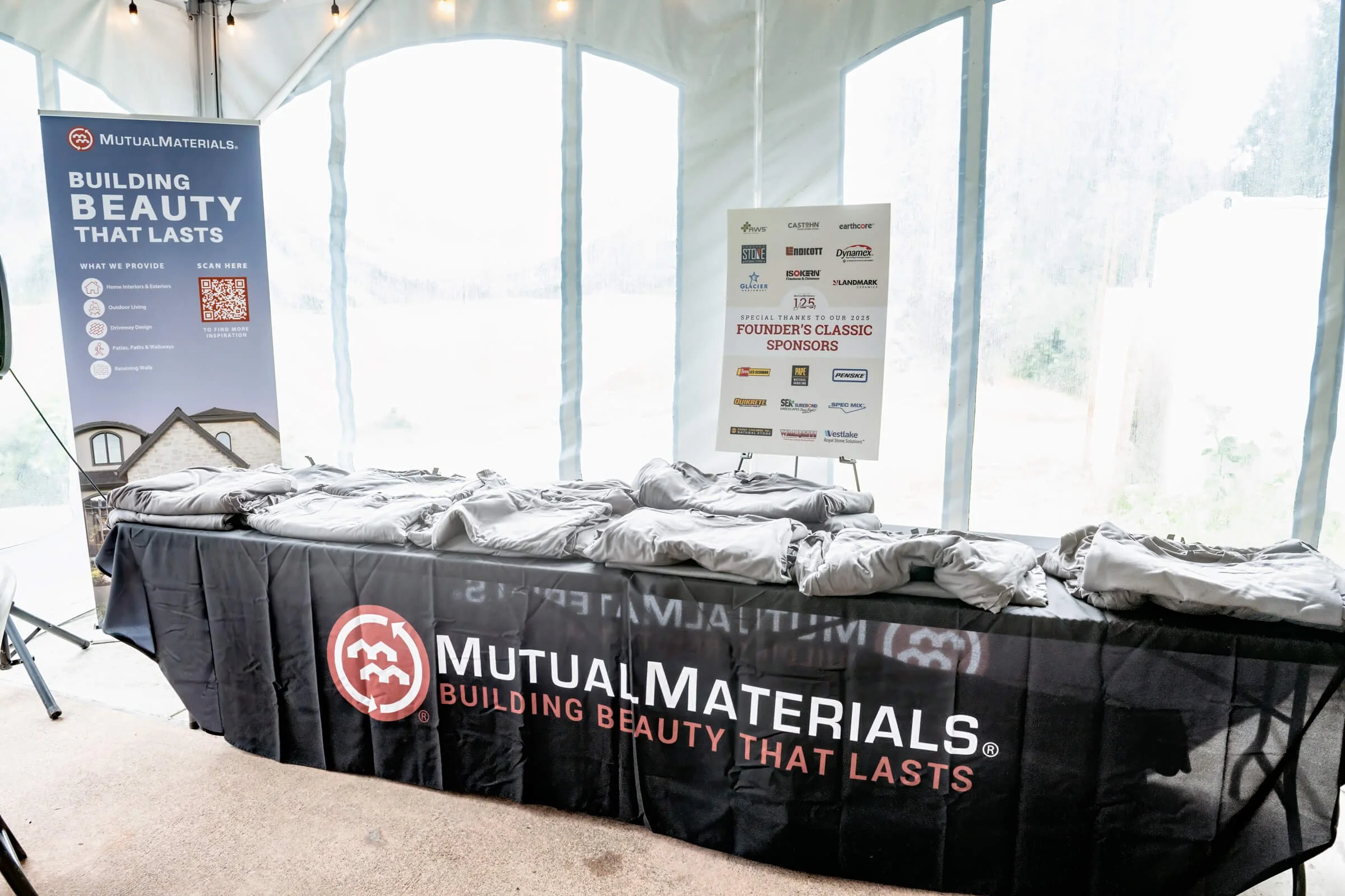 Branded polos displayed for guests, set against sponsor posters and a retractable banner.