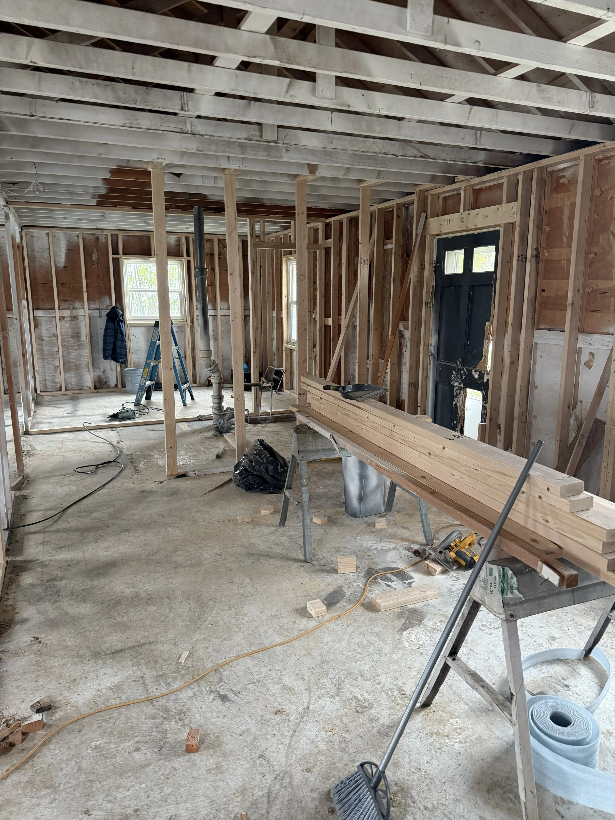 Interior of a house under construction with wooden framing, a worktable with lumber, and construction tools.