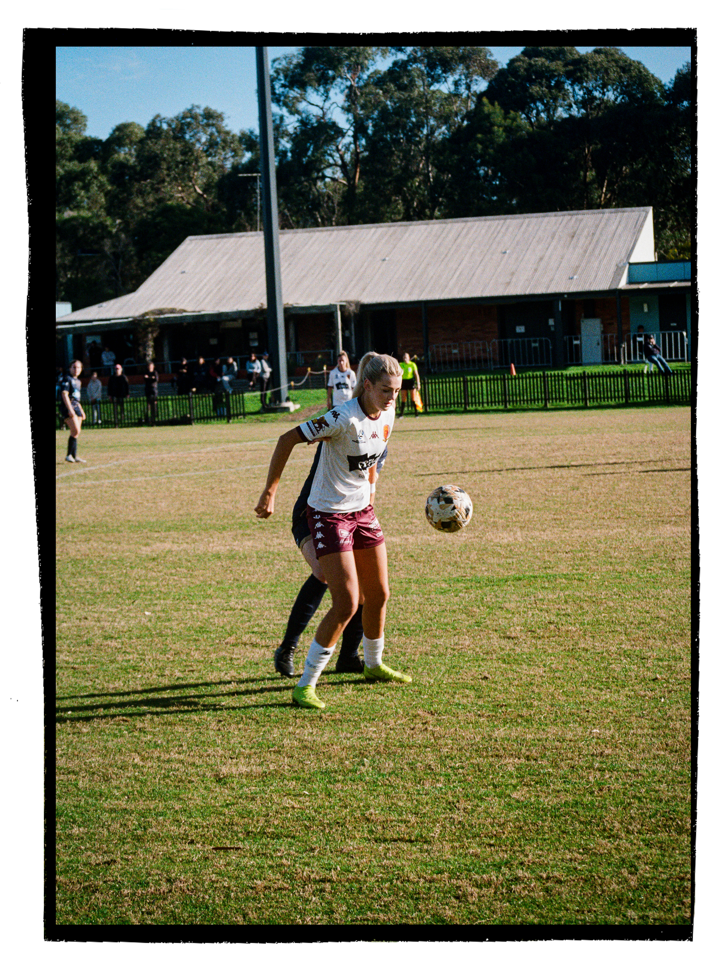 Female soccer player in a white and maroon uniform on a grassy field, playing with a soccer ball.