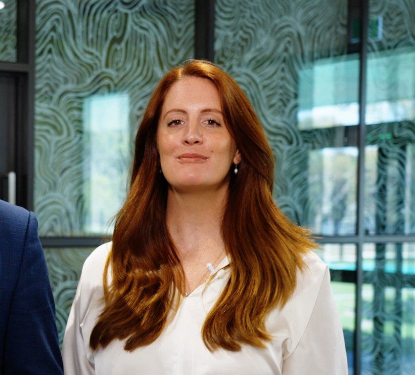 Woman with long red hair wearing a white shirt standing indoors.