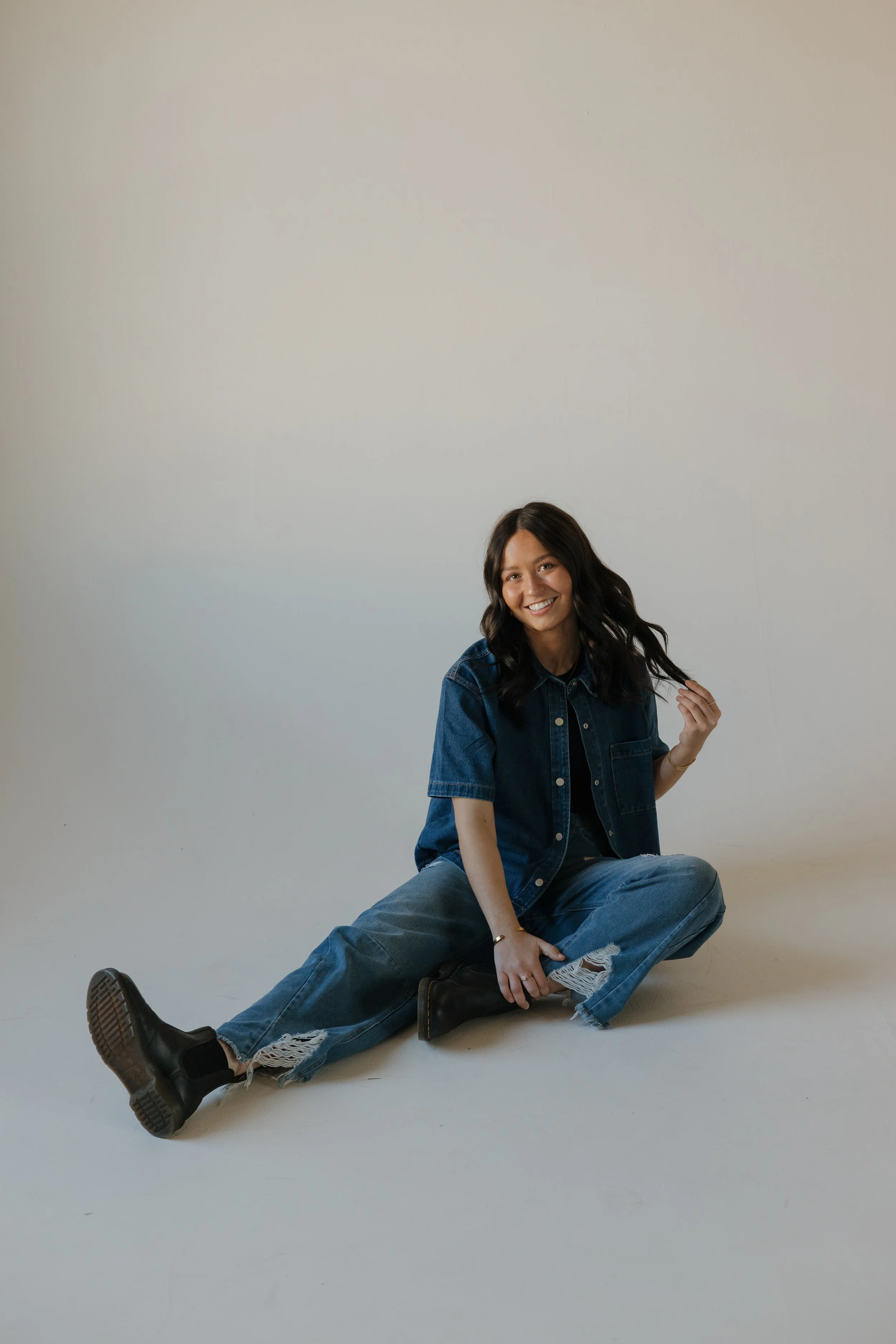 girl sitting on ground holding her hair and smiling at the camera