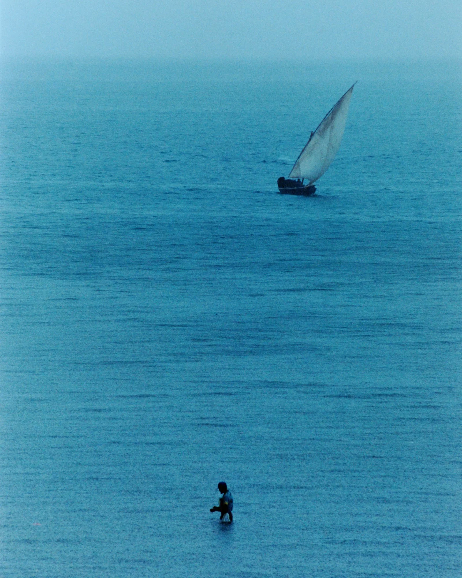 Ocean scene with person wading in water and sailboat sailing away, evoking themes of contact, resilience, and inner journey - core foundation of Erik Rocca Psychotherapy.