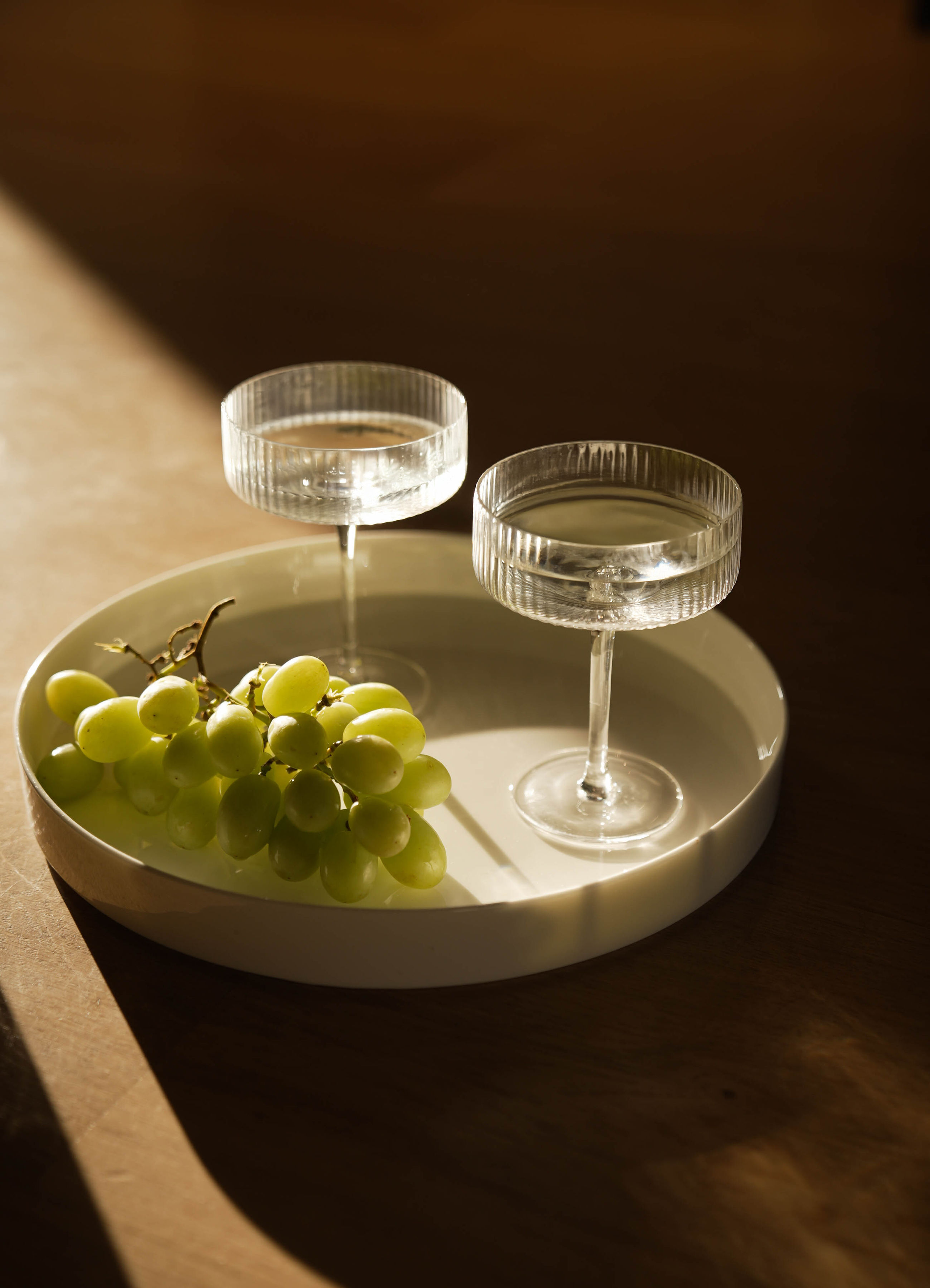 Still life of two crystal glasses and green grapes in warm light representing the selective application standard for private Biological Leadership mentorship.
