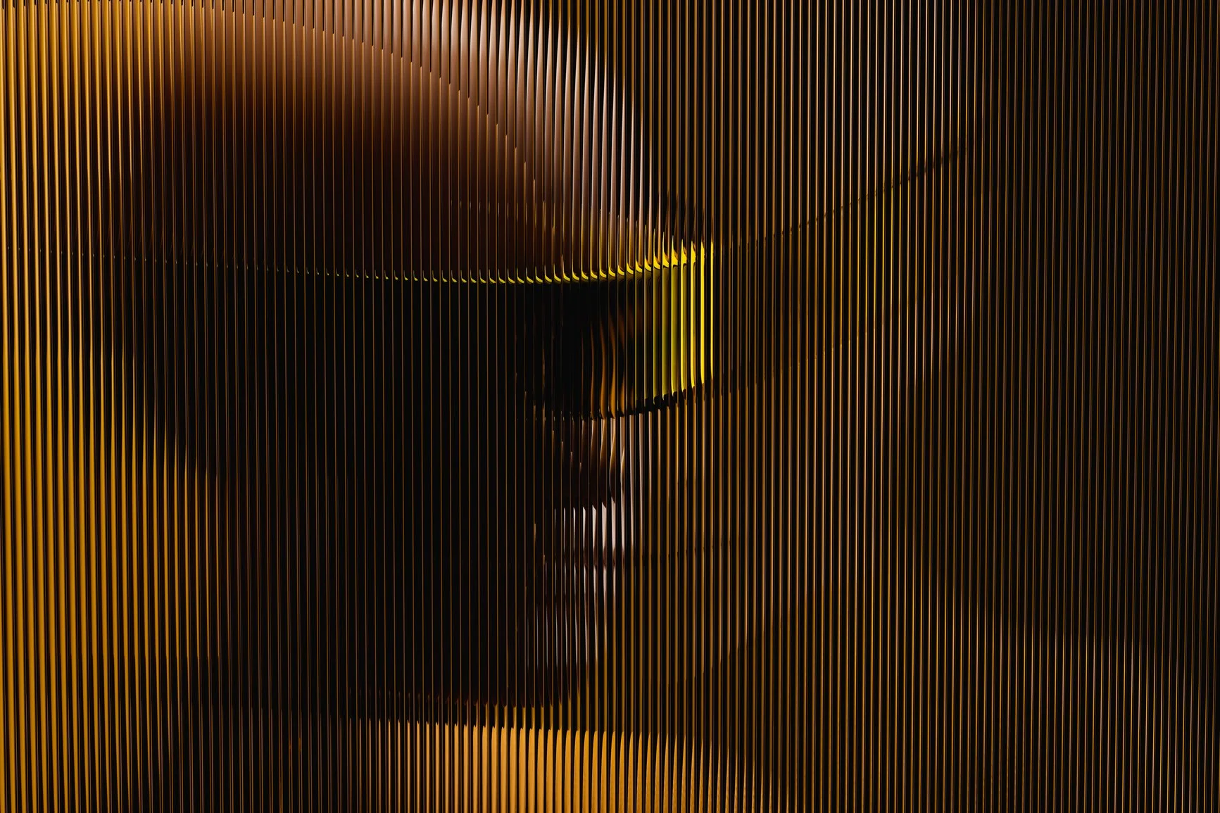 A modern piece of art or installation featuring vertical golden rods creating a partial face outline with eyes and mouth, illuminated with soft lighting.