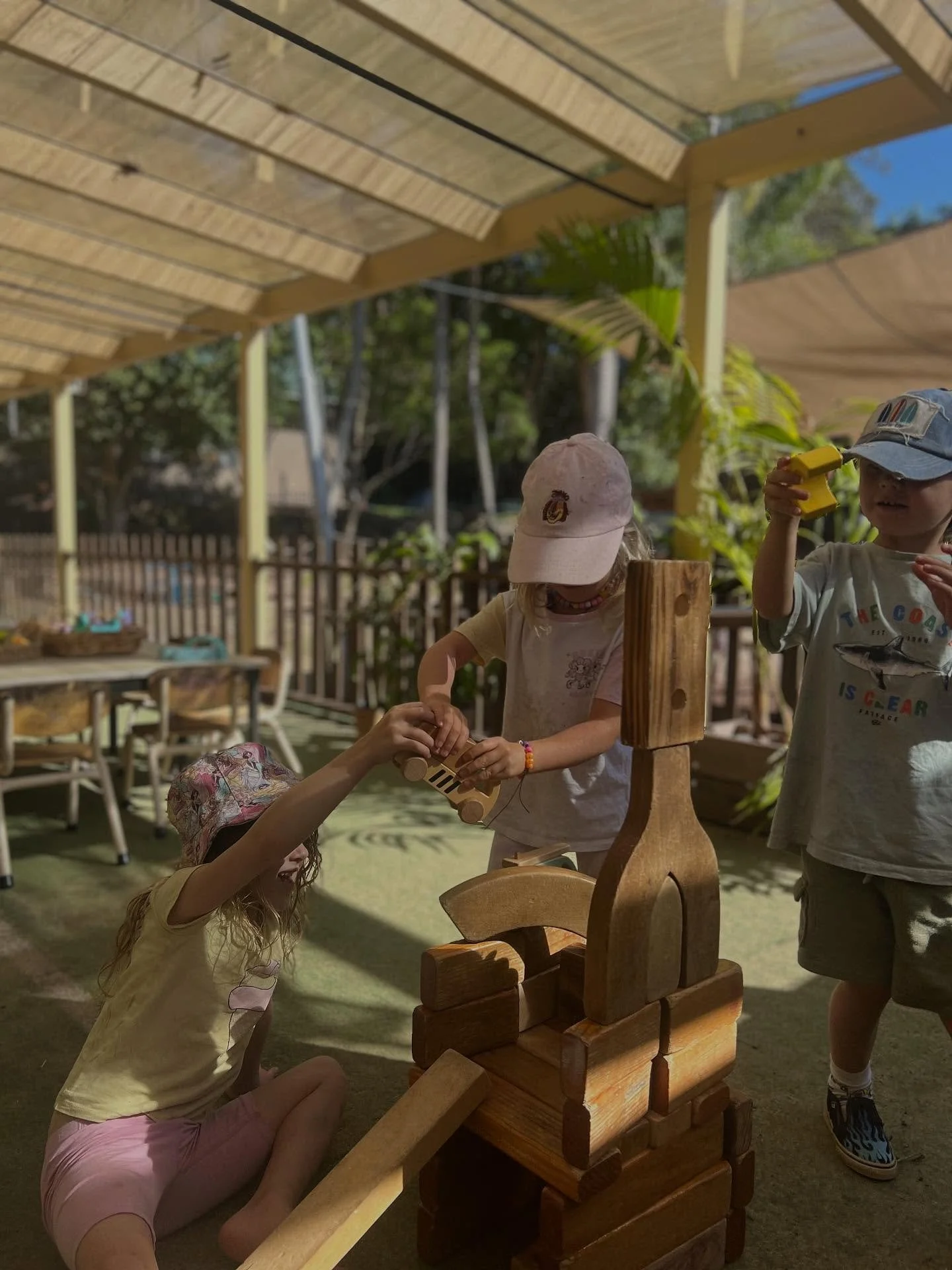 A child in sneakers and a dress on a tire swing at a park, pushed by another child, with green trees and a bench in the background.