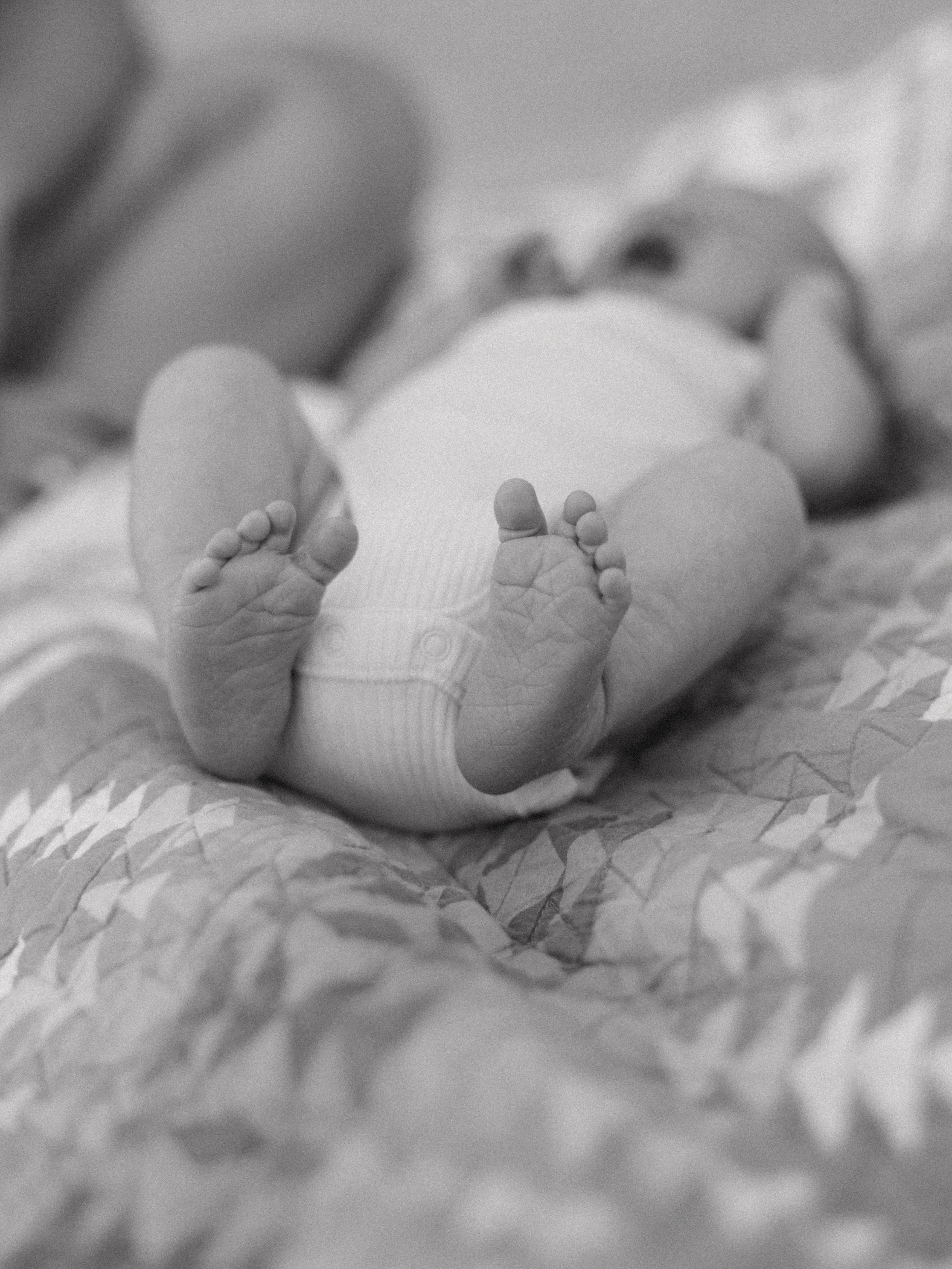 Close-up black and white photo of a newborn baby's feet, with the baby lying on a soft surface.
