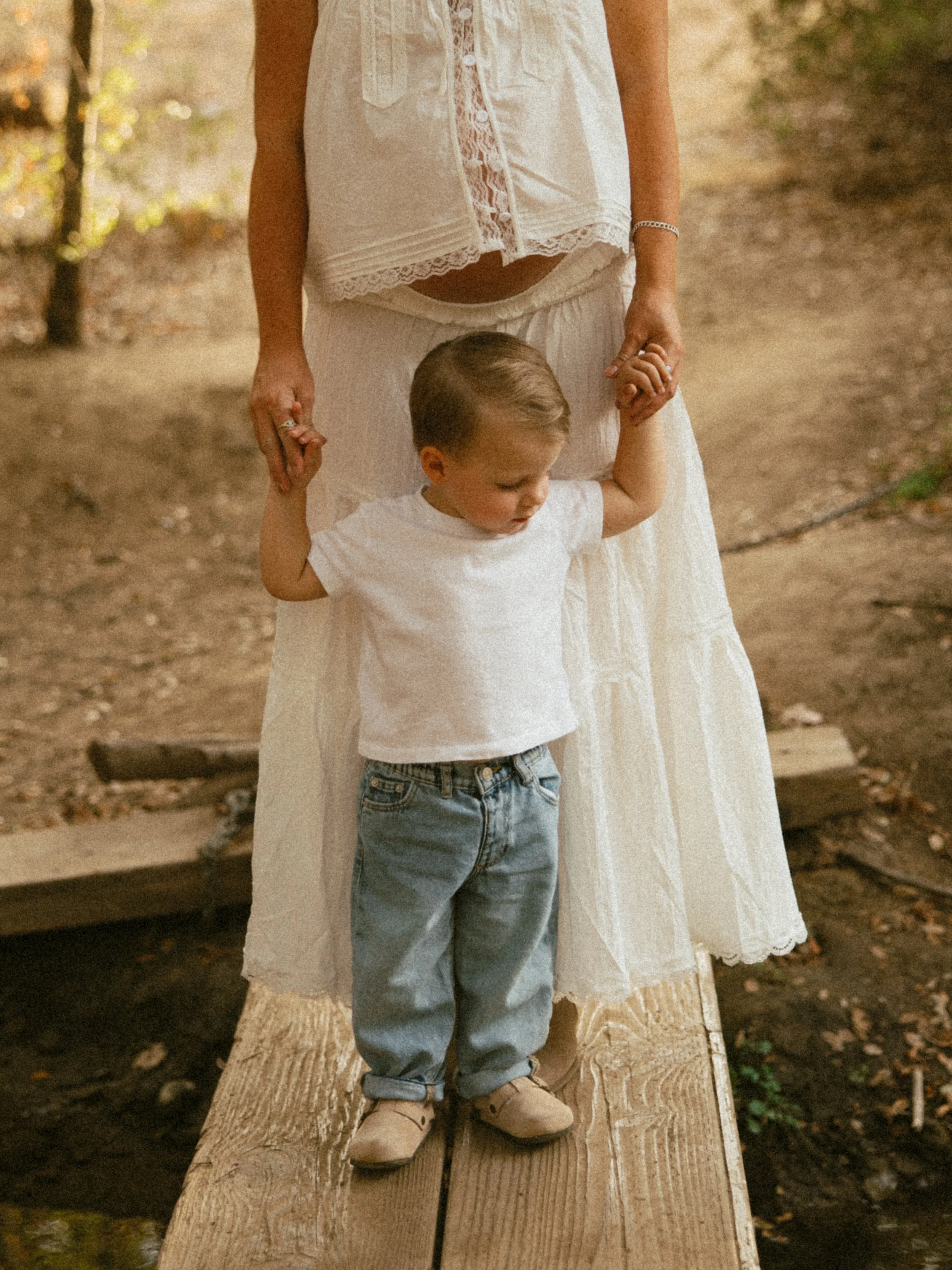 A child holding hands with an adult, standing on a wooden bridge outdoors during daytime.
