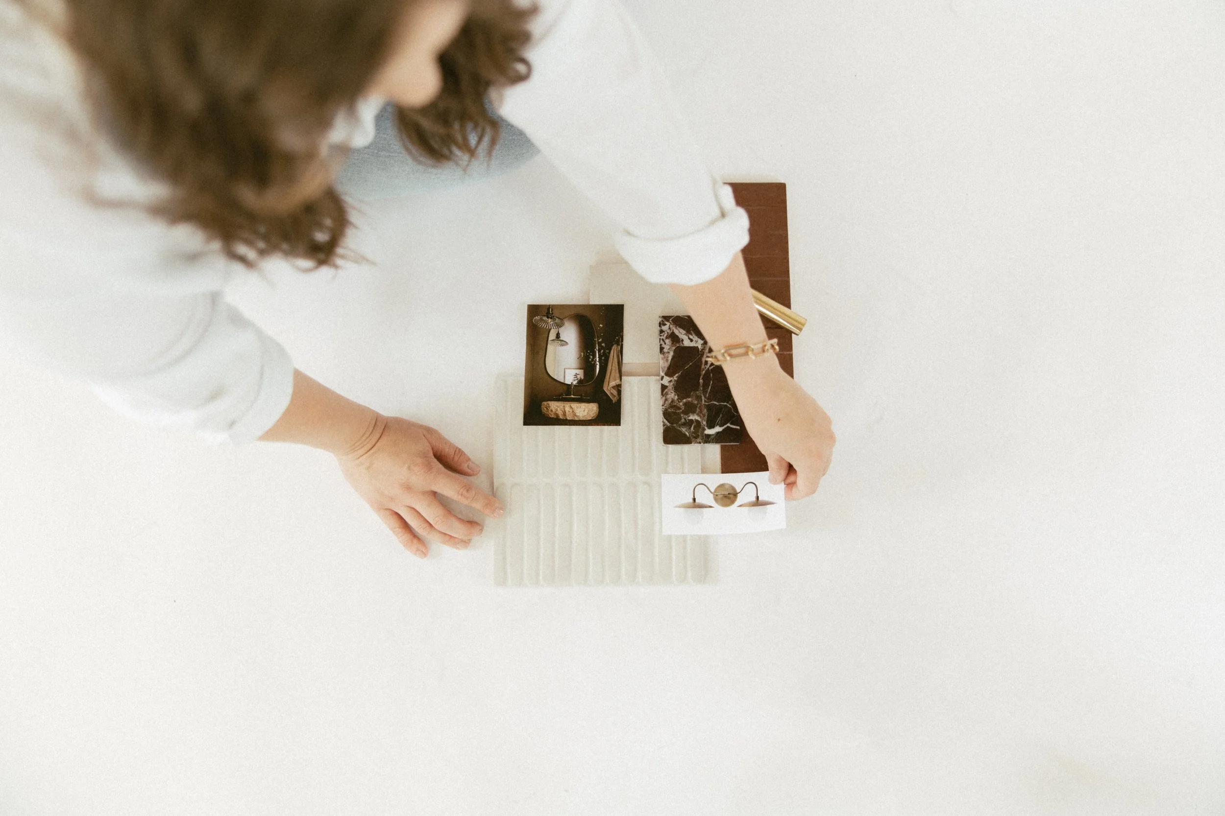 Person placing decorative items on a flat surface with sample images of a sink, a lamp, and a chandelier.
