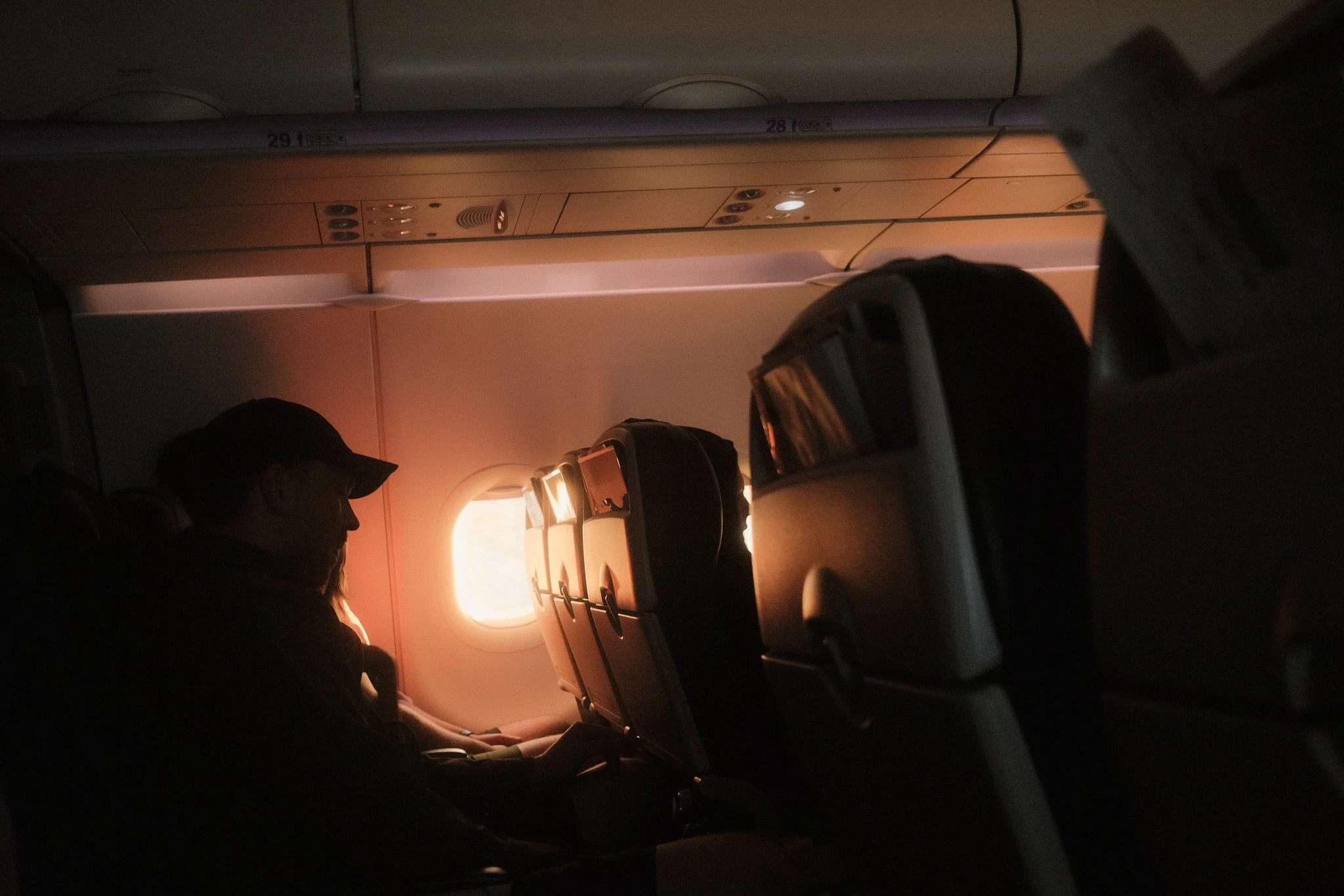 Passengers sitting in airplane seats as the sun sets outside the window.