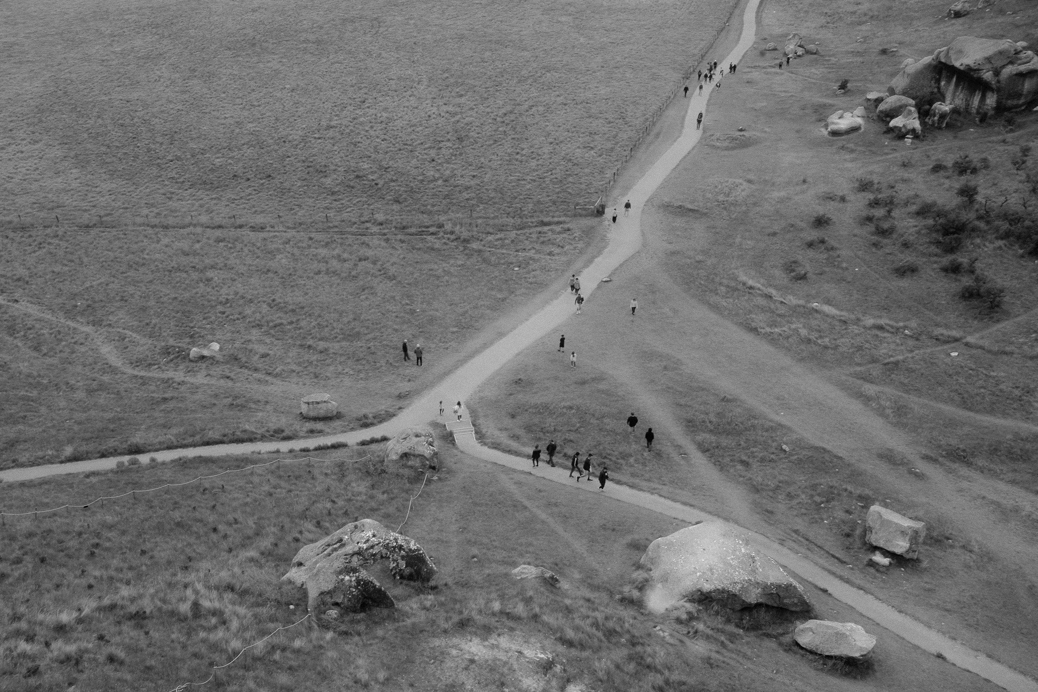 Aerial view of a winding walking trail across a grassy landscape with large rocks and people walking along the path.