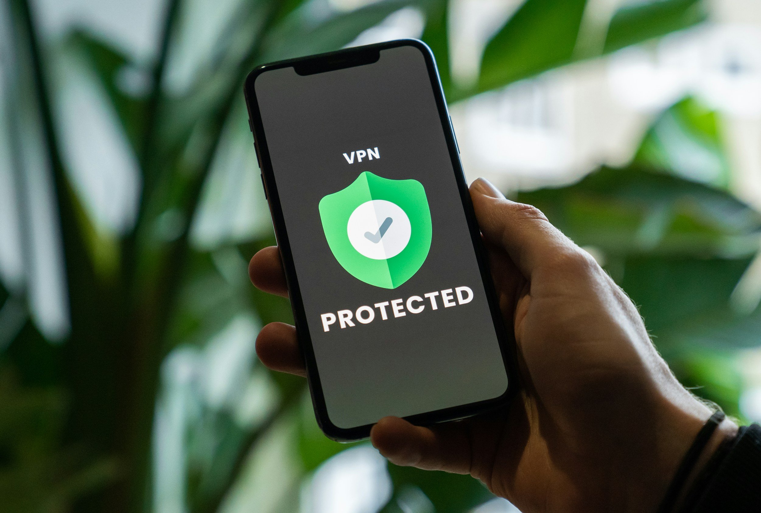 A person holding a smartphone with a VPN protection icon on the screen, showing a green shield with a checkmark and the words 'VPN PROTECTED'.