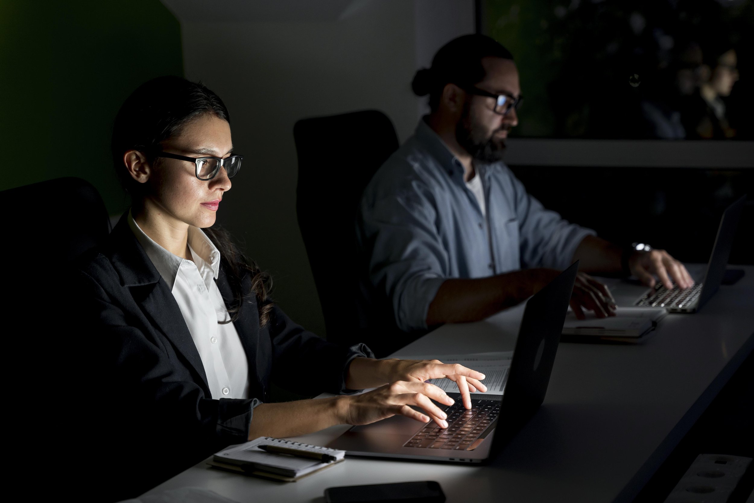 People working on laptops in a darkened room during a meeting or presentation.