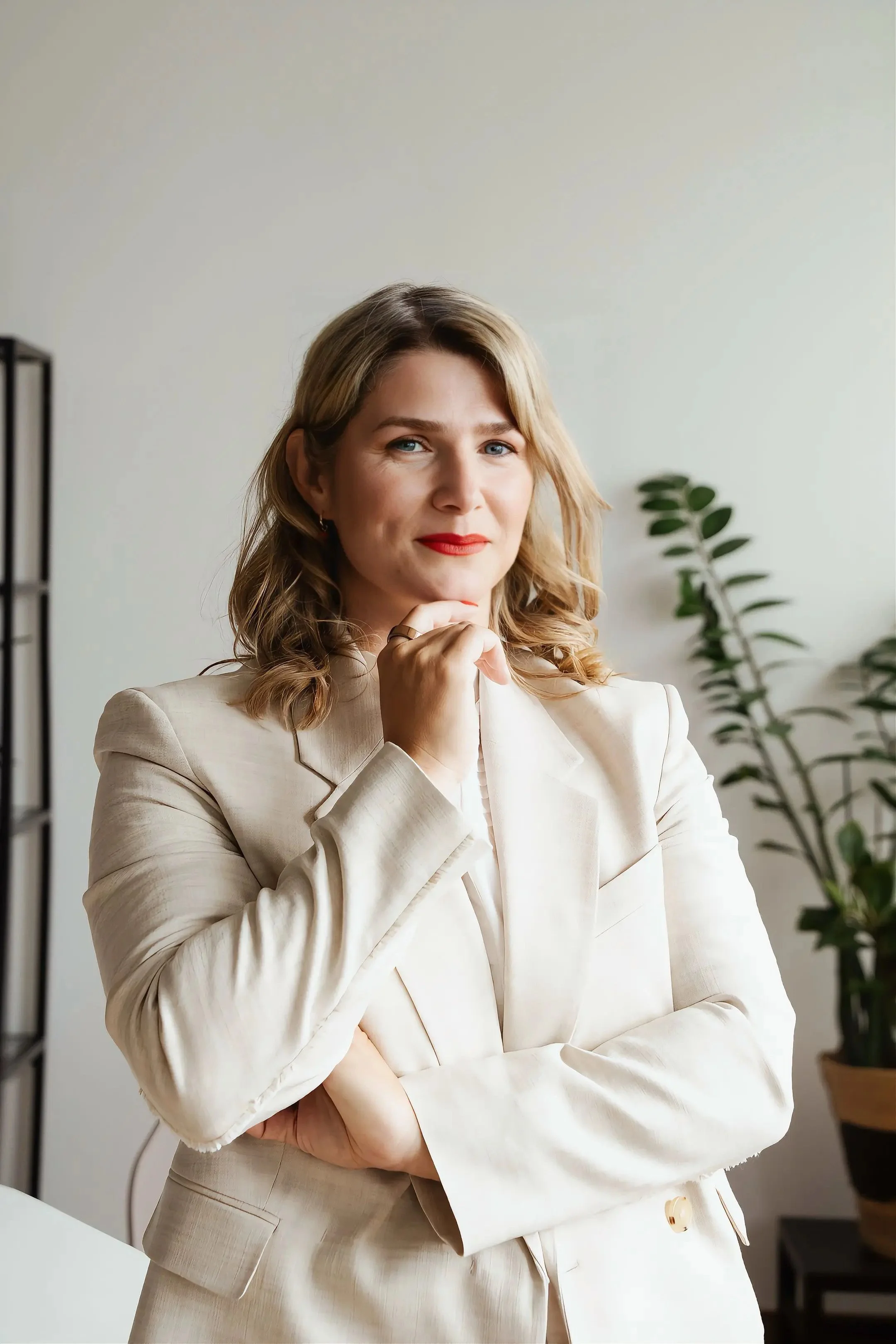 An image of Zeljka Cacic-Escalera, a GLP-1 and Transformation Coach in Oceanside, California. She has blonde hair, blue eyes, and red lipstick, wearing a cream-colored blazer, standing in an office.