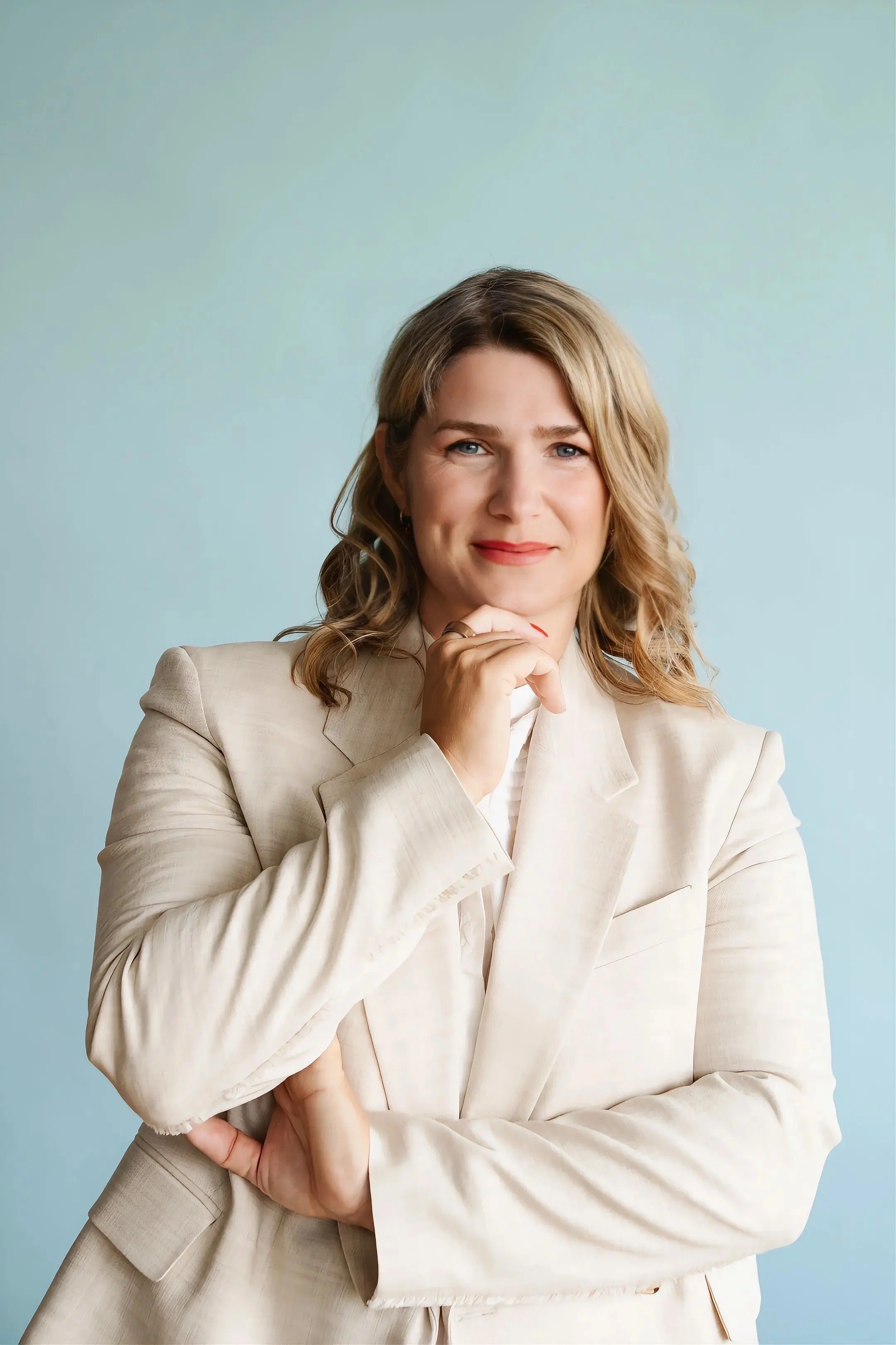 An image of Zeljka Cacic-Escalera, a GLP-1 and Transformation Coach in Oceanside, California. She has blonde, wavy hair, wearing a cream-colored blazer, poses against a light blue background.
