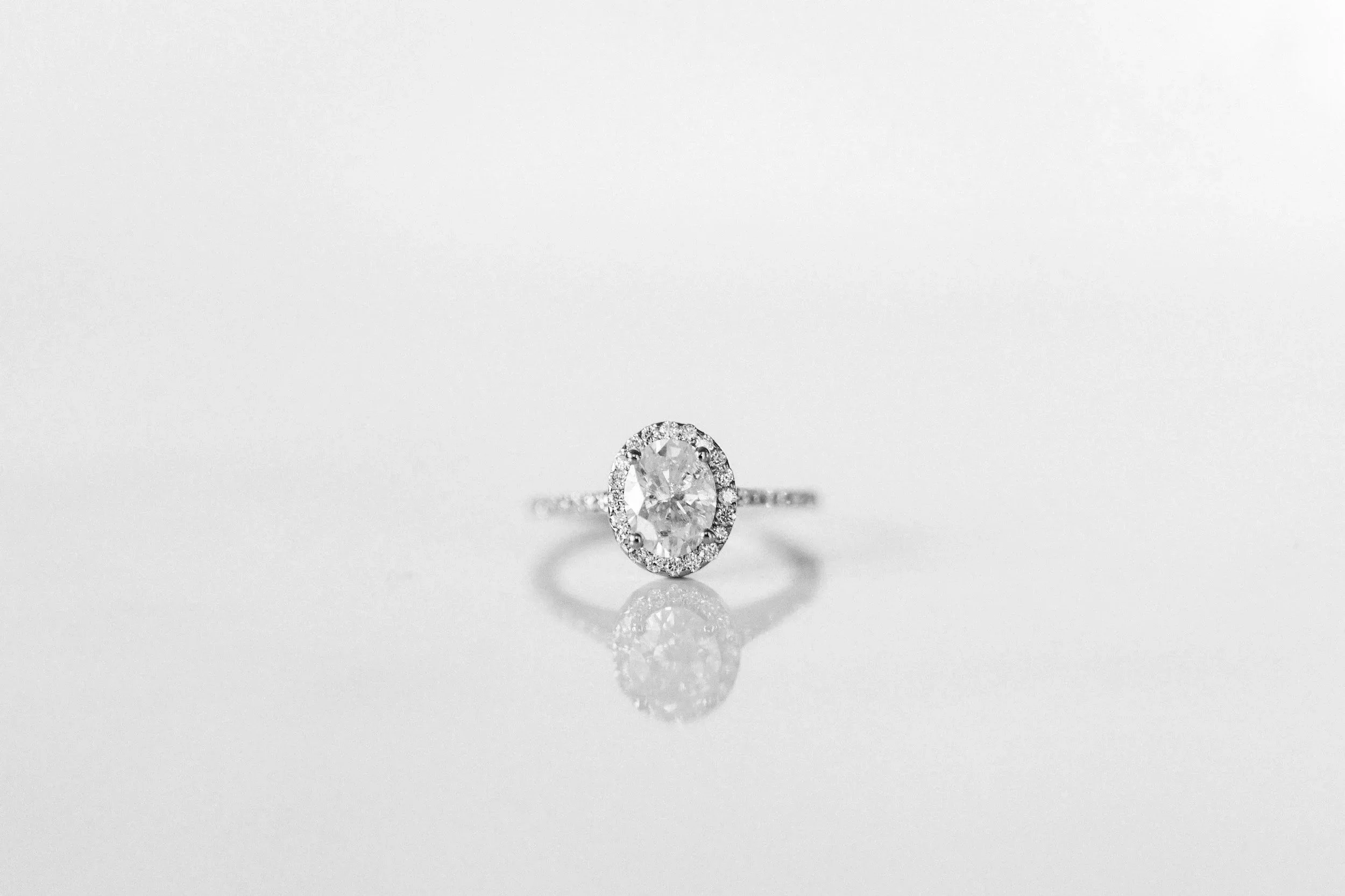 Elegant diamond engagement ring with a central oval diamond surrounded by smaller diamonds on a simple band, photographed on a white background.