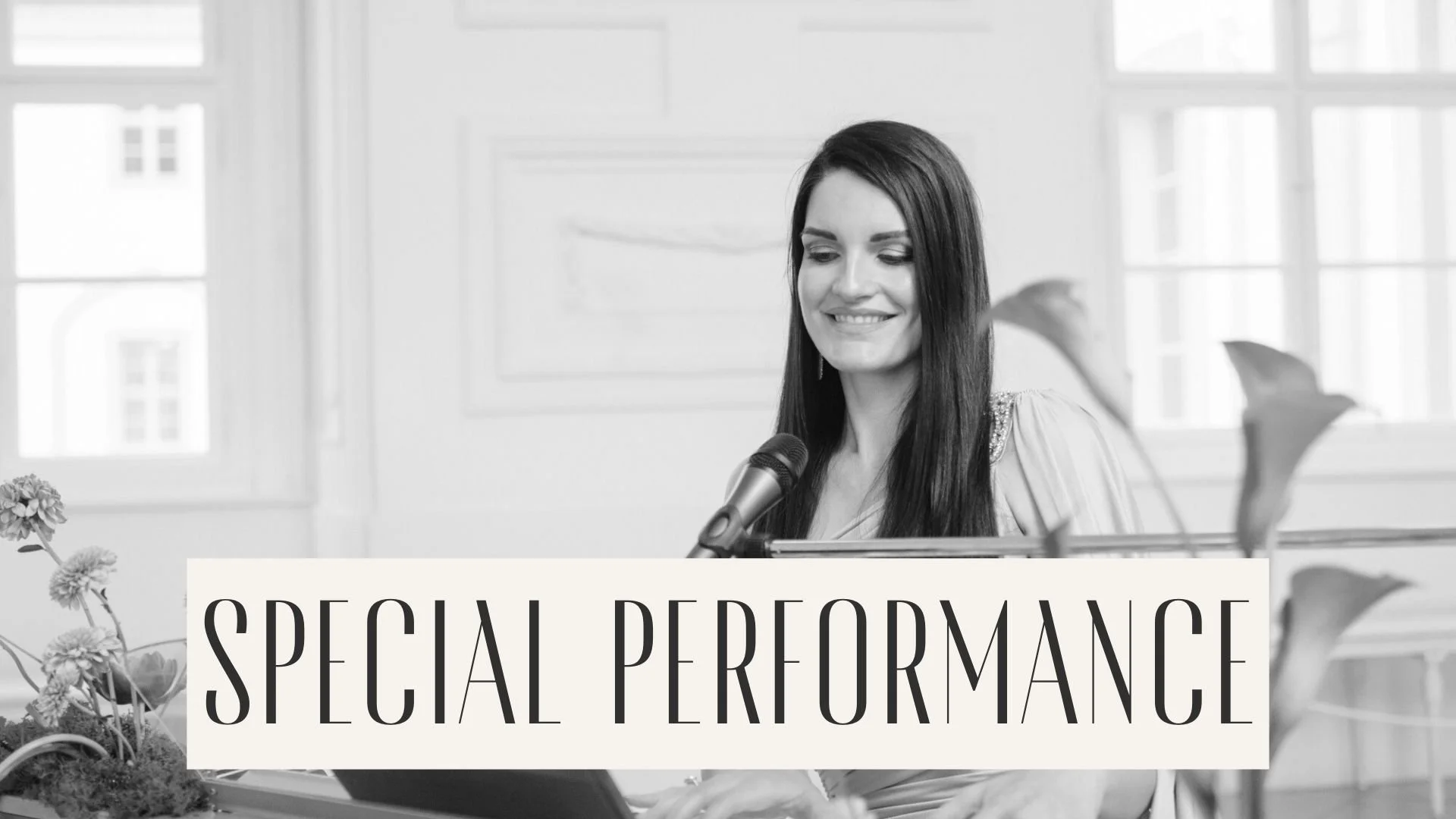 A woman smiling and singing into a microphone with a keyboard in front of her, with a sign reading 'Special Performance' at the bottom, in a bright room with large windows.