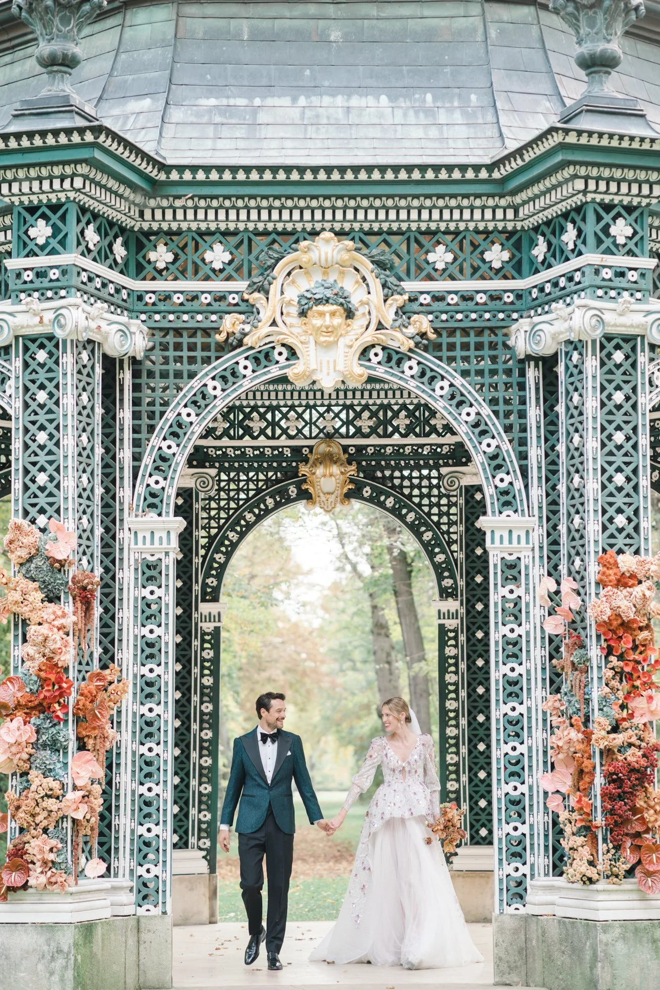 A bride and groom walking hand in hand through an ornate archway decorated with pink flowers, after their wedding ceremony. This luxurious wedding couple is accompanied by a unique wedding music with piano and vocals.