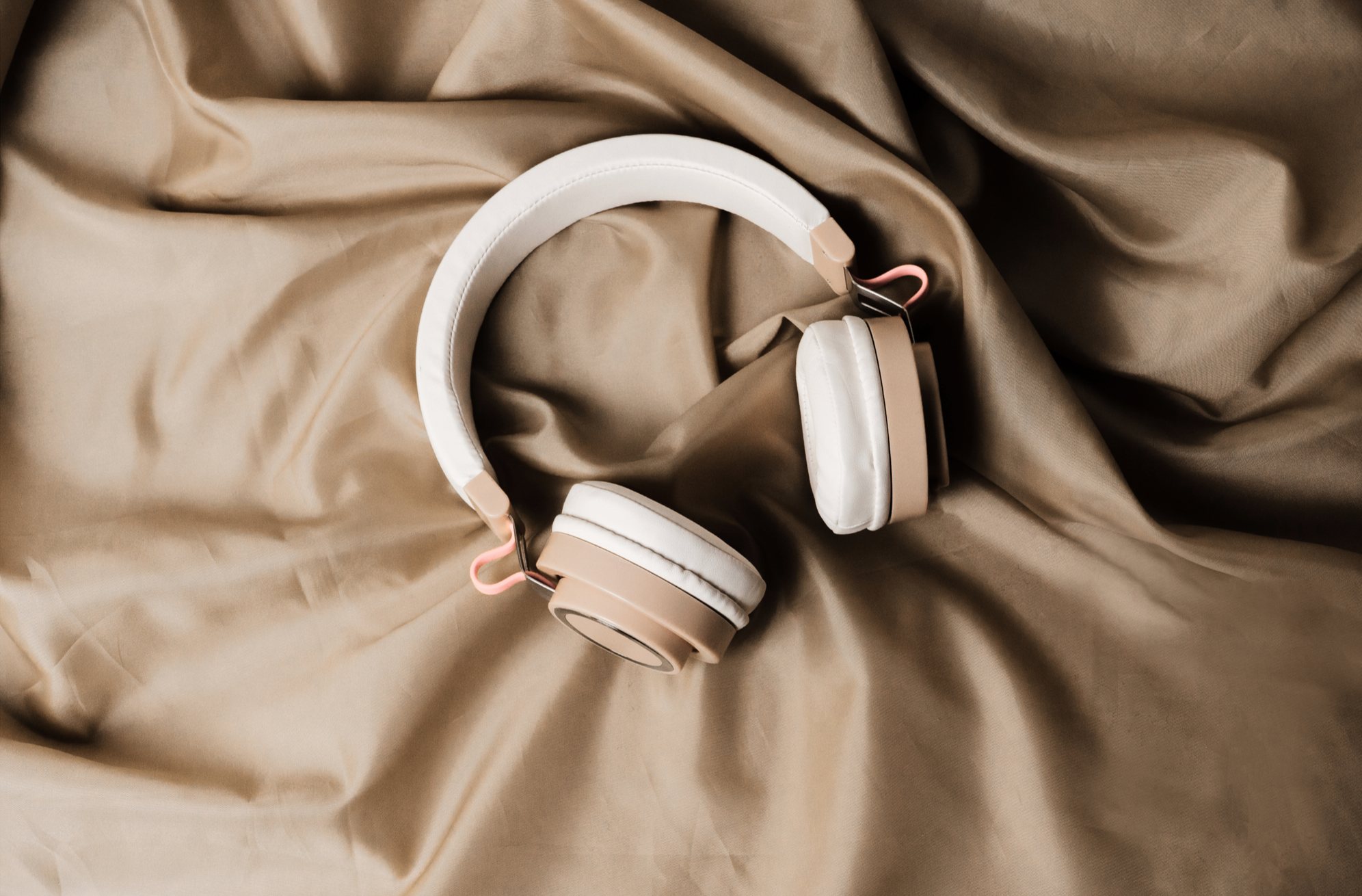 A pair of beige and white over-ear headphones resting on tan fabric.