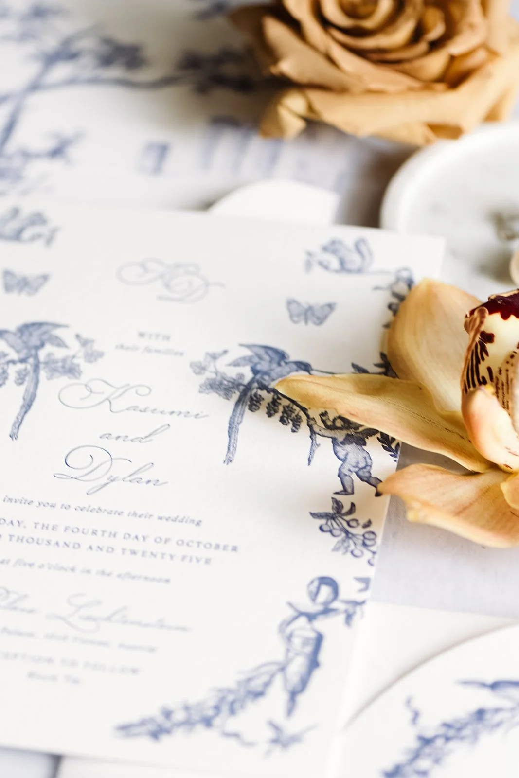 Close-up of a wedding invitation with floral and butterfly illustrations, with dried roses and petals nearby.