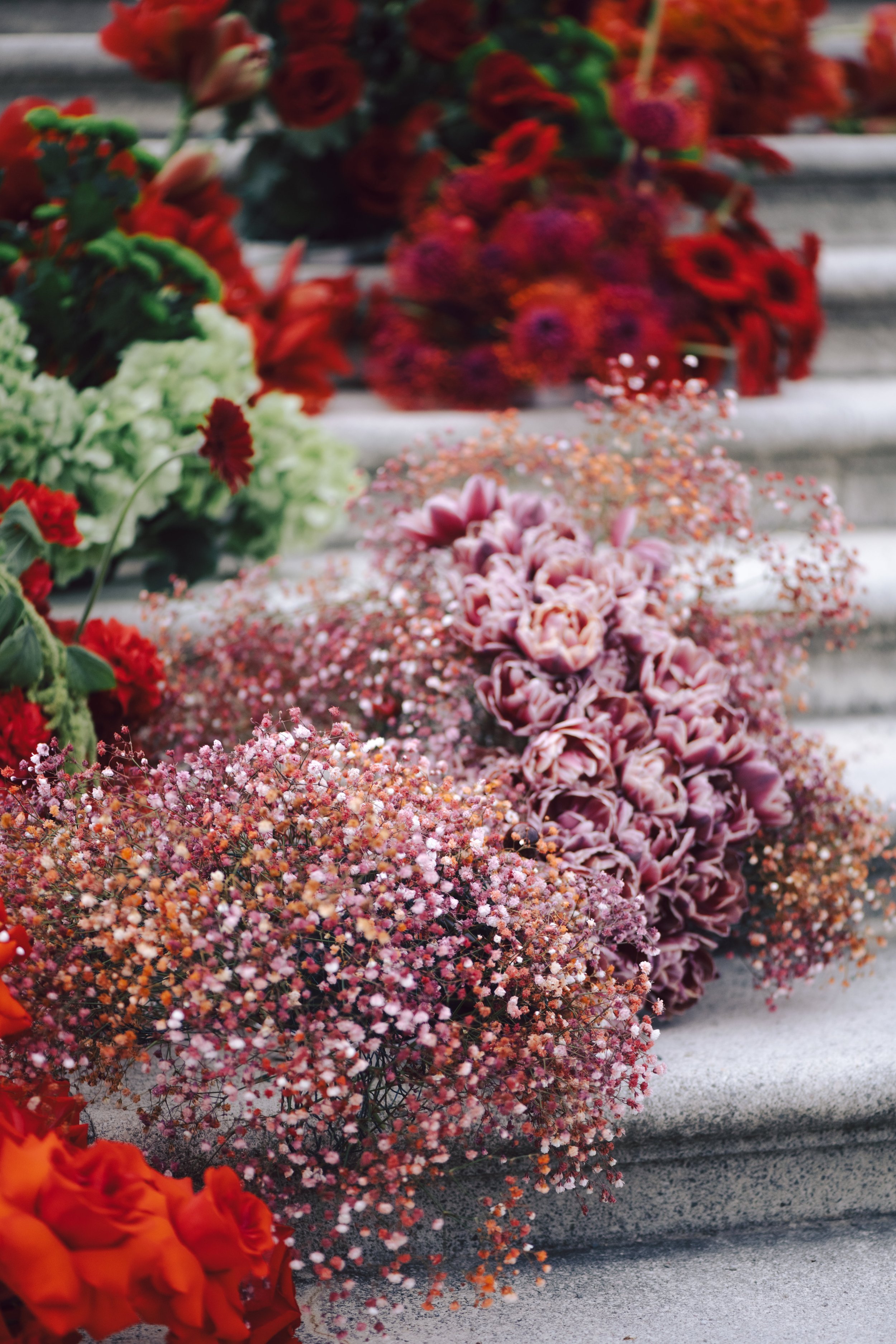Colorful floral arrangements with pink, red, purple, and white flowers displayed on concrete steps.