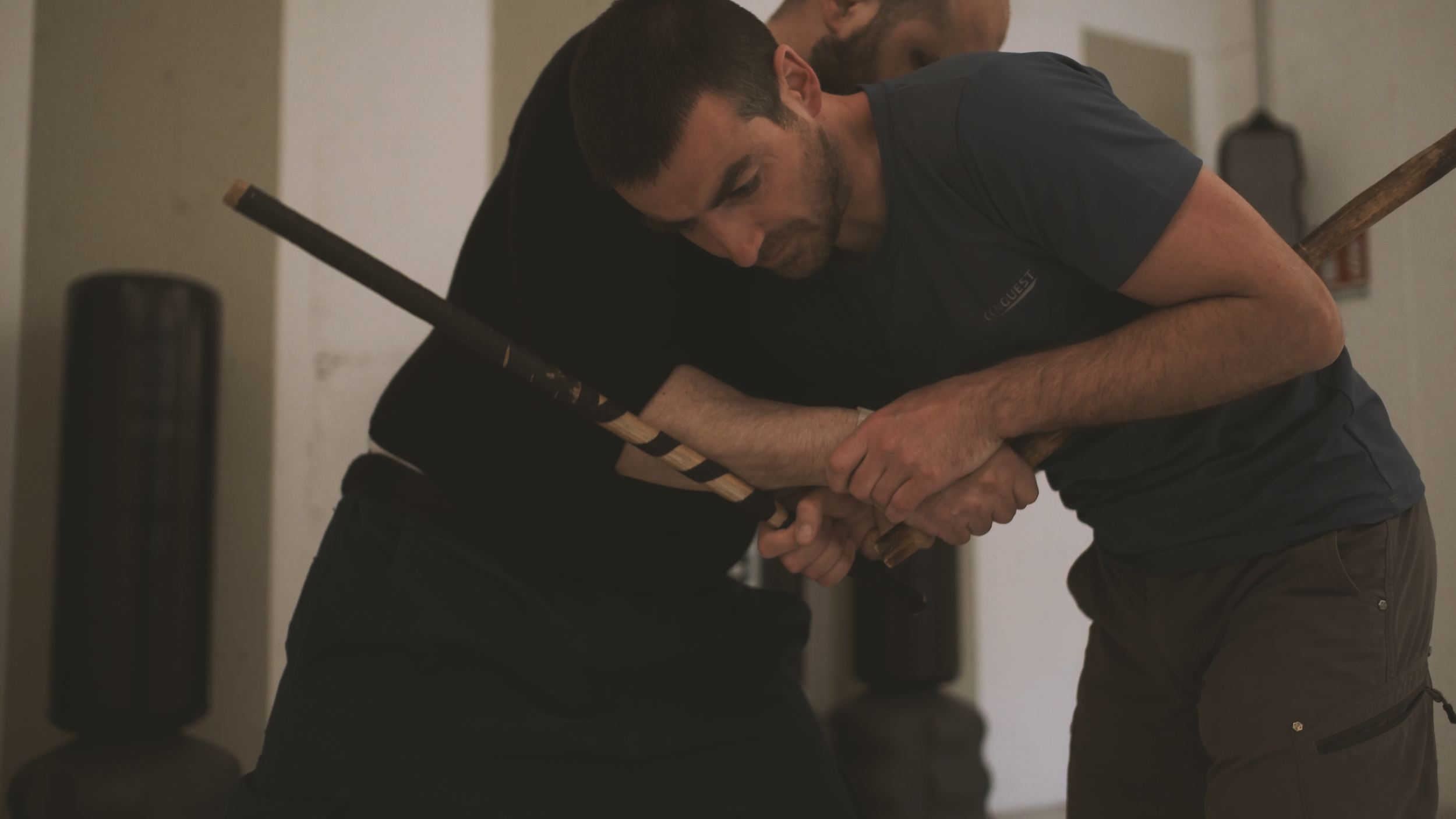 Zwei Männer kämpfen mit Stöcken in einem Raum