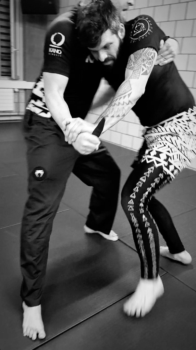 Zwei Männer beim Brazilian Jiu-Jitsu im Trainingsraum, einer demonstriert einen Griff am anderen.