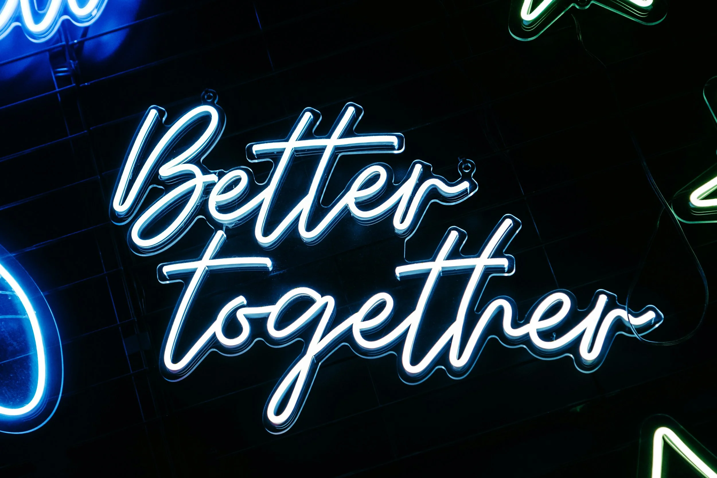 Neon sign displaying the phrase 'Better together' in blue and white letters on a dark background.