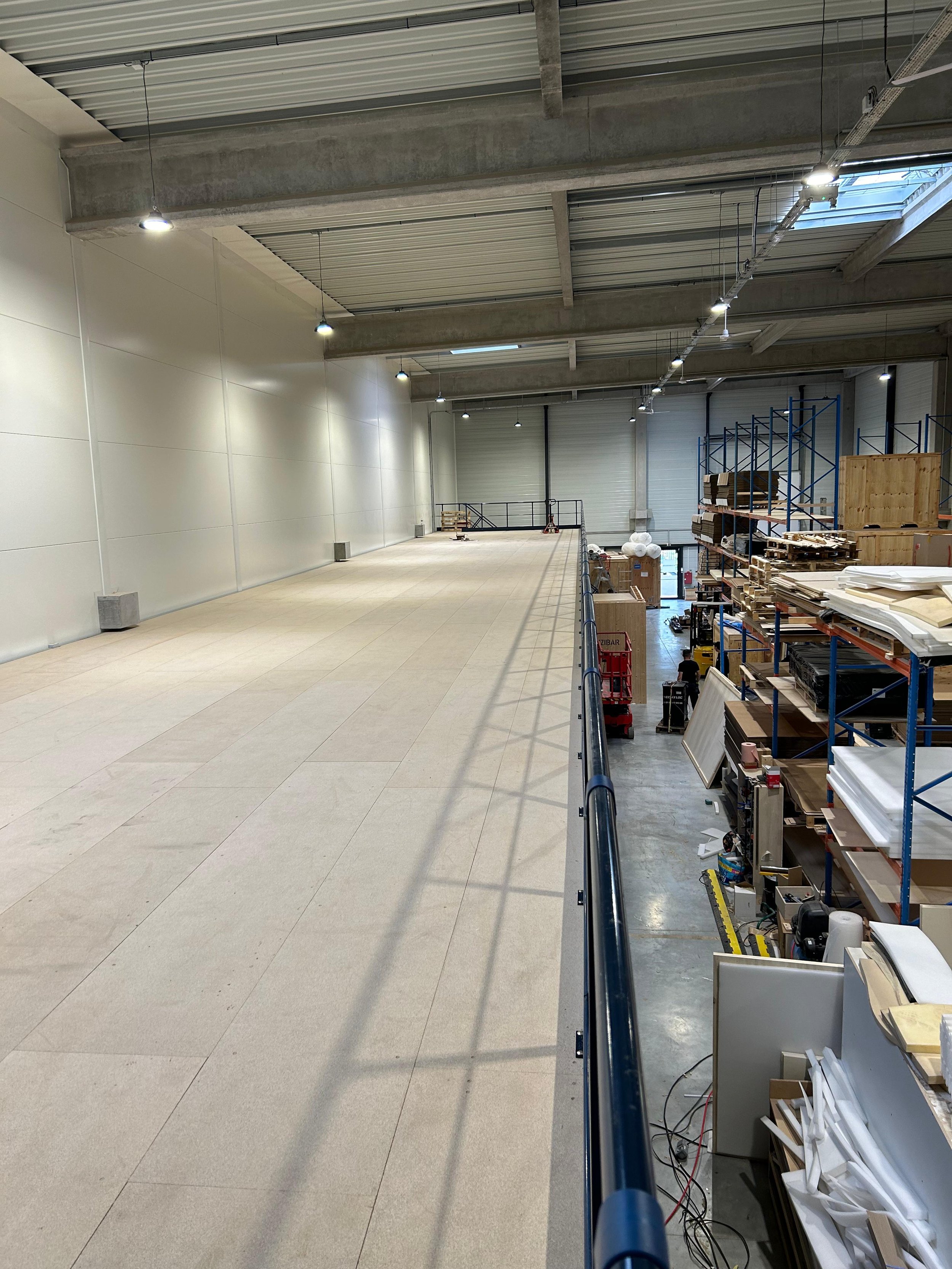 Intérieur d'un entrepôt en cours de montage avec des étagères en métal, du matériel, et une zone dégagée au centre.