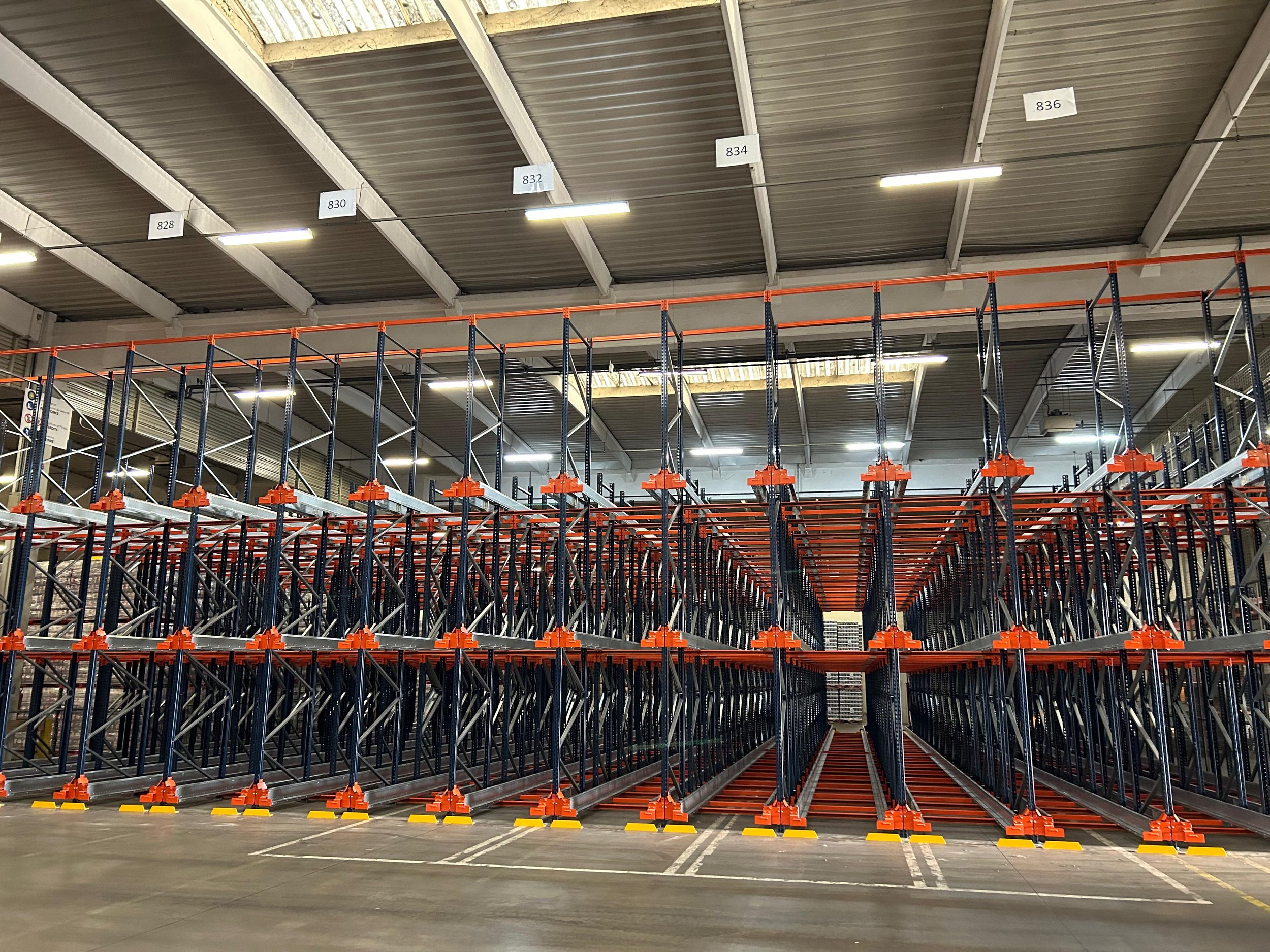 Rayonnage industriel vide avec plusieurs niveaux, marqué par des étiquettes numérotées sur le plafond, dans un entrepôt