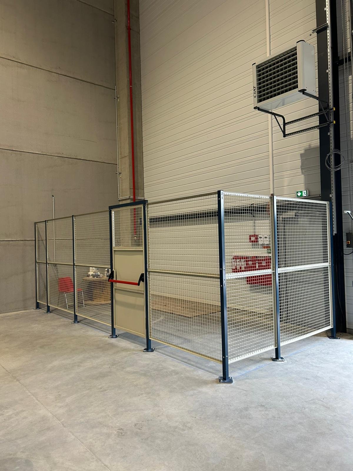 Zone de sécurité avec clôture métallique entourant une plateforme élévatrice avec un ascenseur intégrée, dans une grande salle industrielle