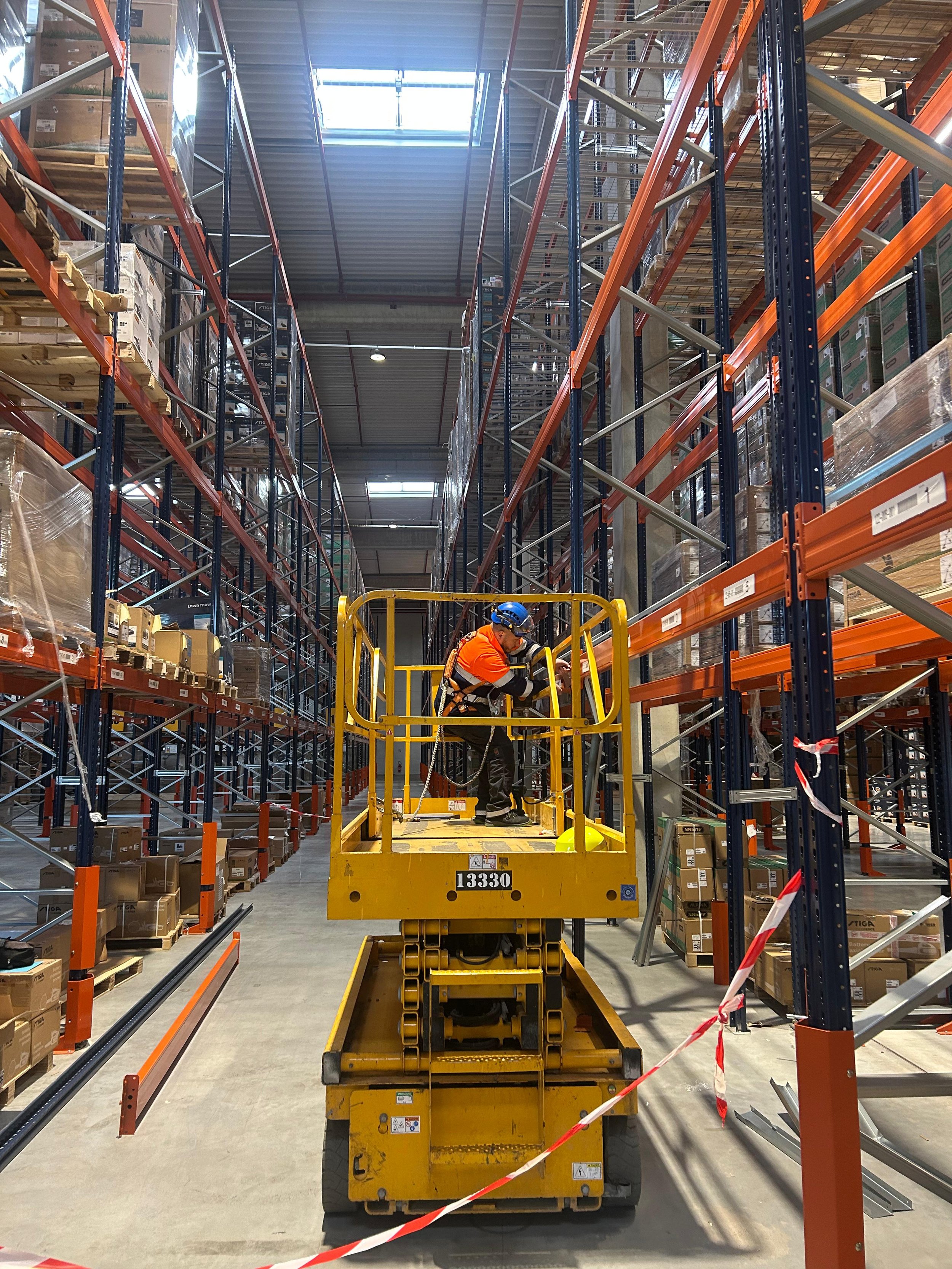 Technicien utilisant une plateforme élévatrice dans un entrepôt de stockage, avec des rayonnages remplis de cartons.