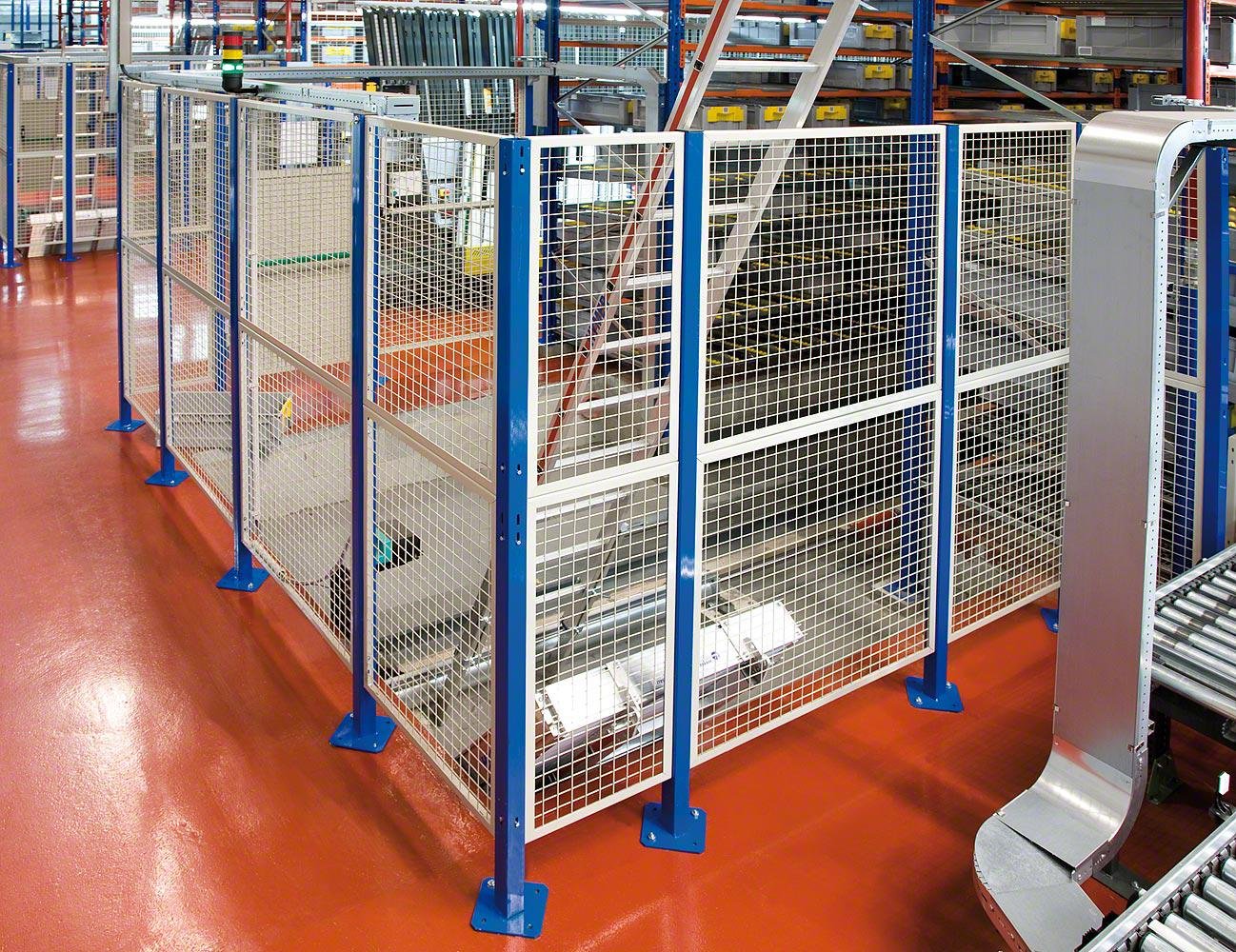 Zone de sécurité dans un entrepôt industriel avec des barrières métalliques bleues, un escalier en arrière-plan et une surface de sol en résine rougeâtre.