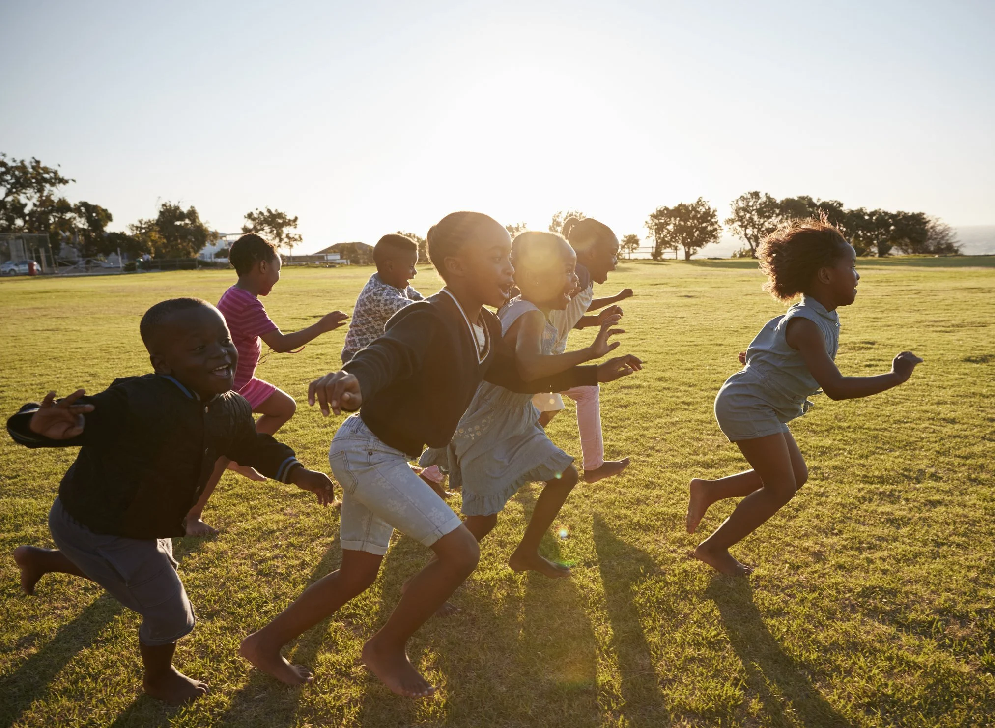 Children running on a grassy field during sunset