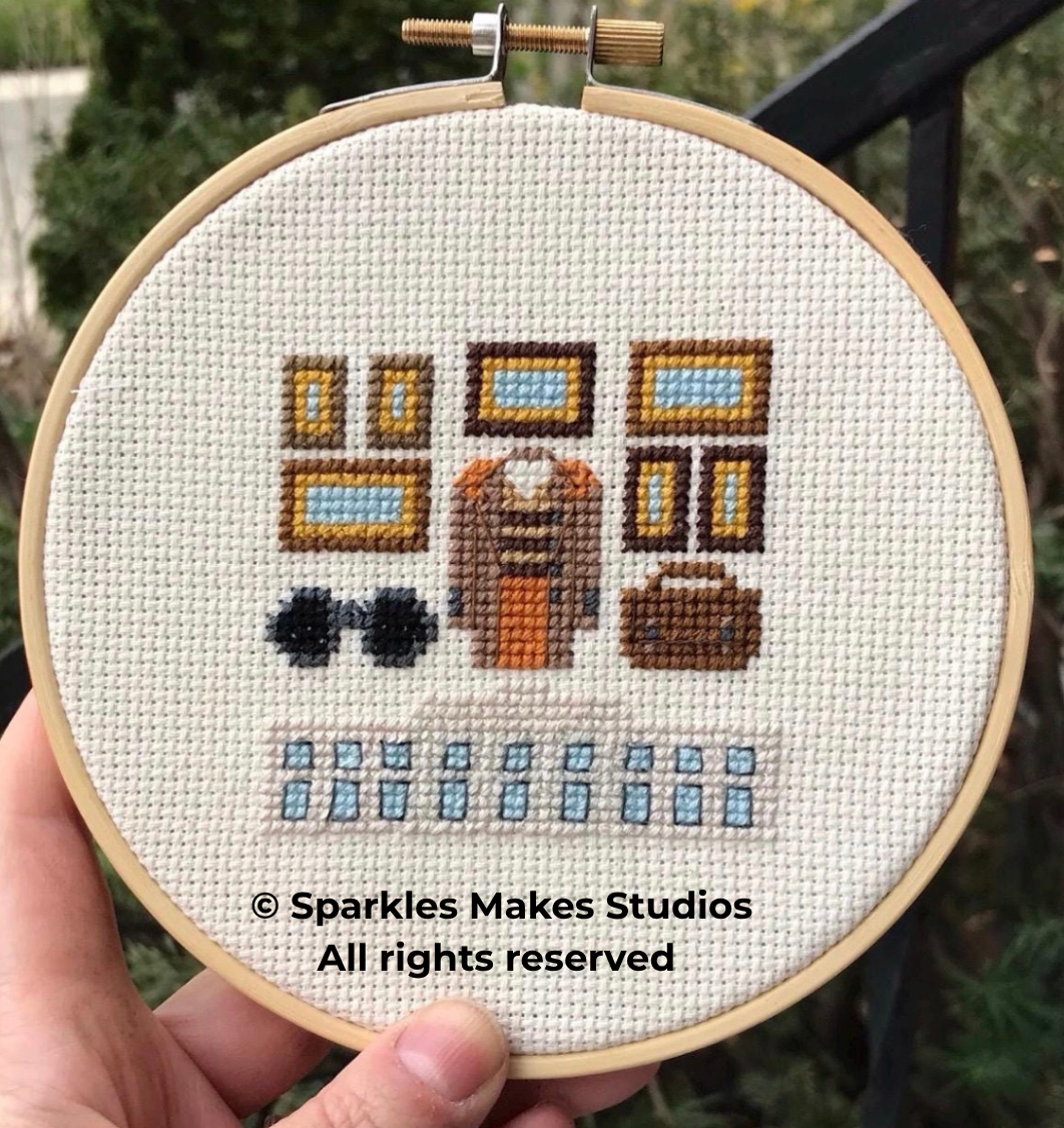 Cross-stitch embroidery of a person's wardrobe including sunglasses, a person's torso, a suitcase, and shelves with picture frames, all in pixel art style.