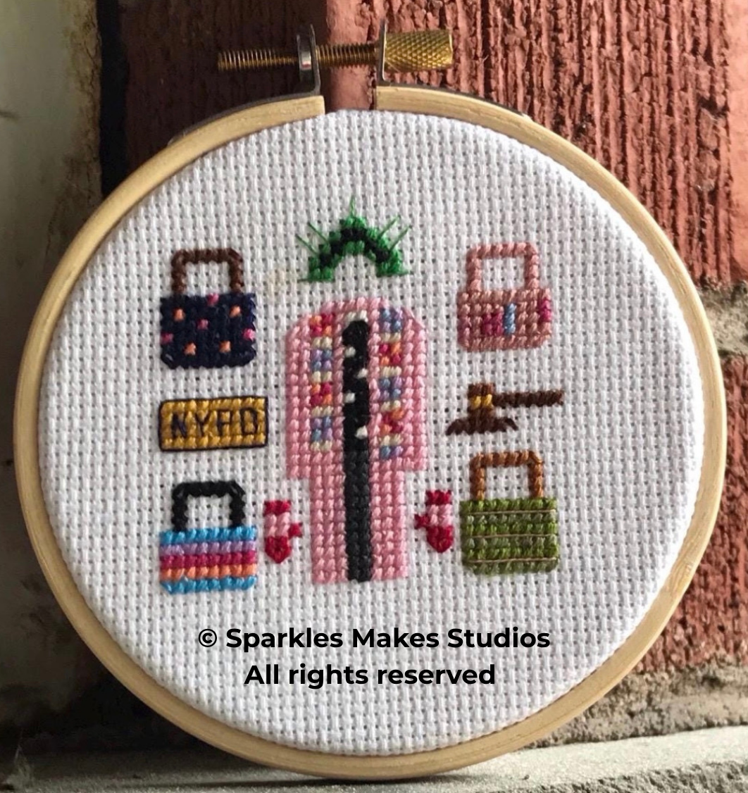 Cross-stitch embroidery of a vintage payphone surrounded by various bags and accessories, with a copyright notice for Sparkles Makes Studios.