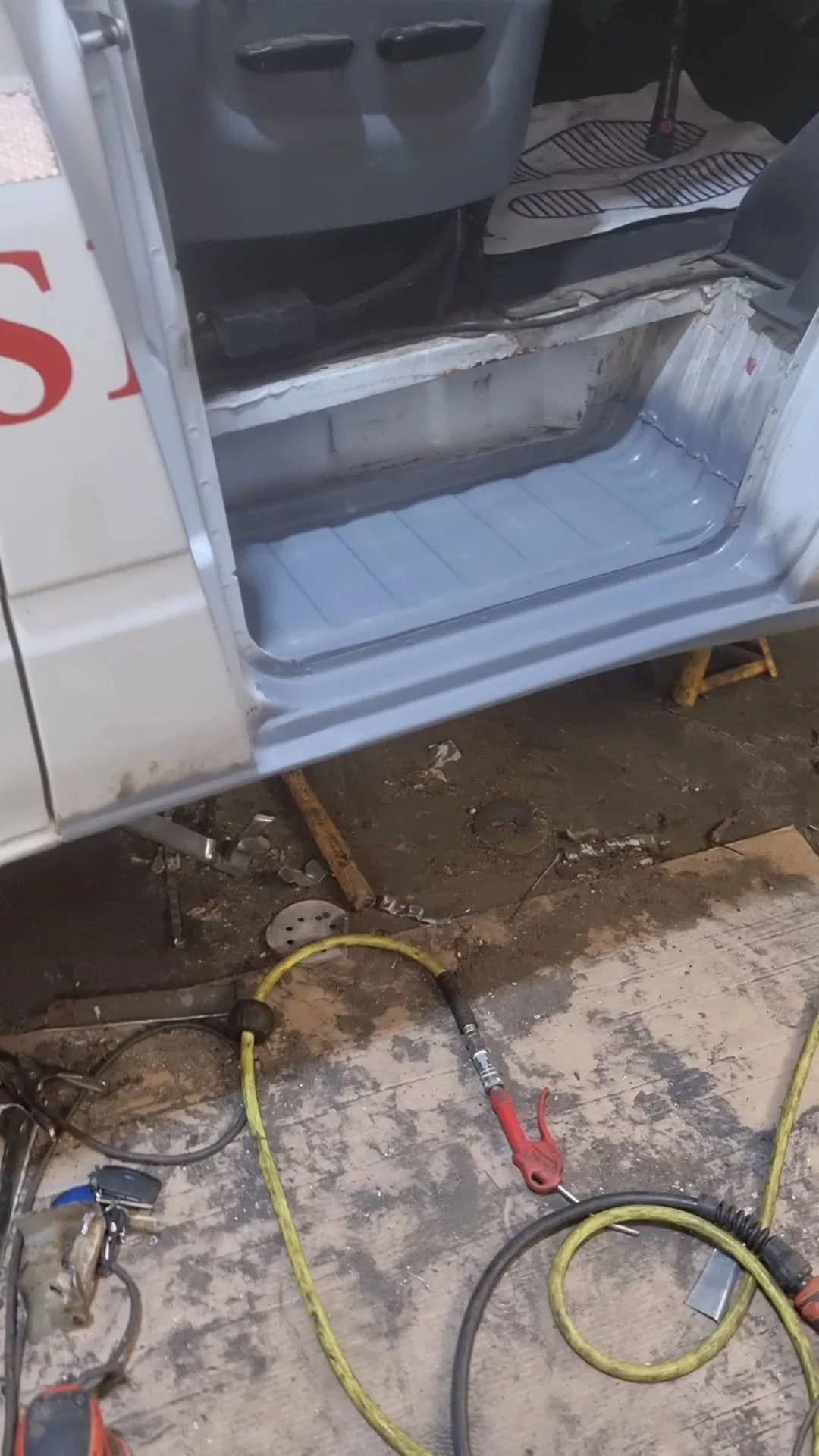 Partially disassembled vehicle interior, showing the inner frame and floor with some wiring and tools on the concrete ground.