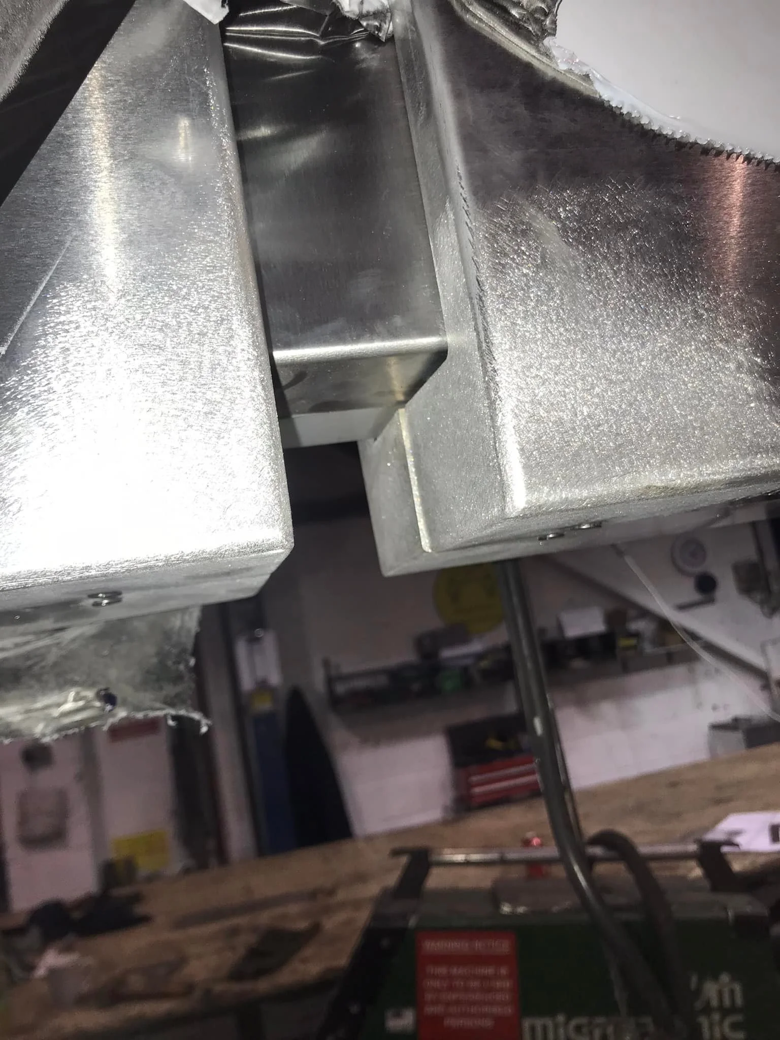 Close-up of a metallic machine part or component in a workshop setting, with tools and equipment in the background.