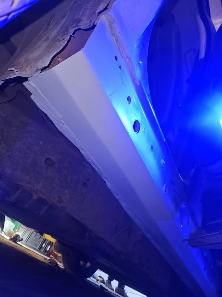 Underneath view of a vehicle with a newly installed illuminated blue LED light strip along the side. The vehicle is raised, revealing the undercarriage and a glimpse of the wheel.