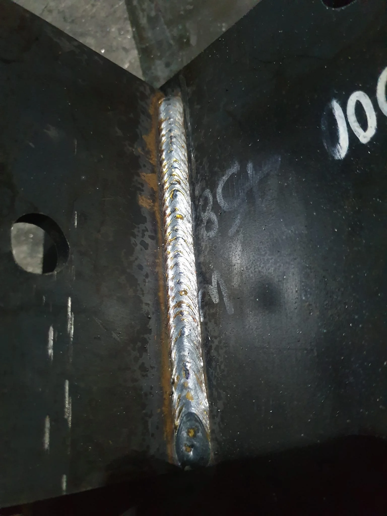 Close-up of a welded metal joint on a black metal piece, showing a shiny, evenly welded seam.