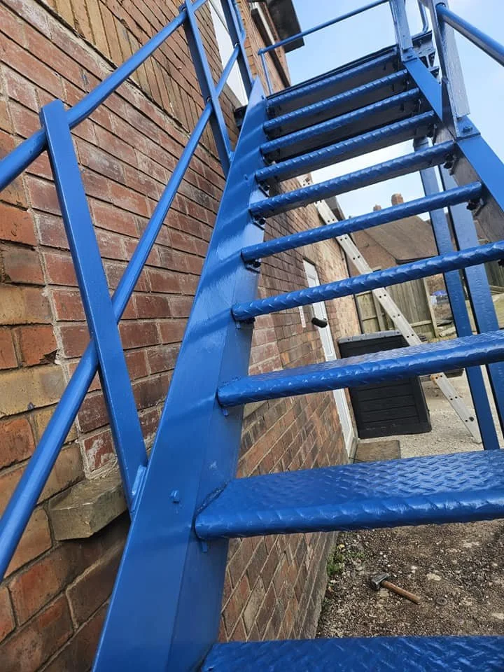 A blue metal exterior staircase attached to a brick building, seen from below at an upward angle.