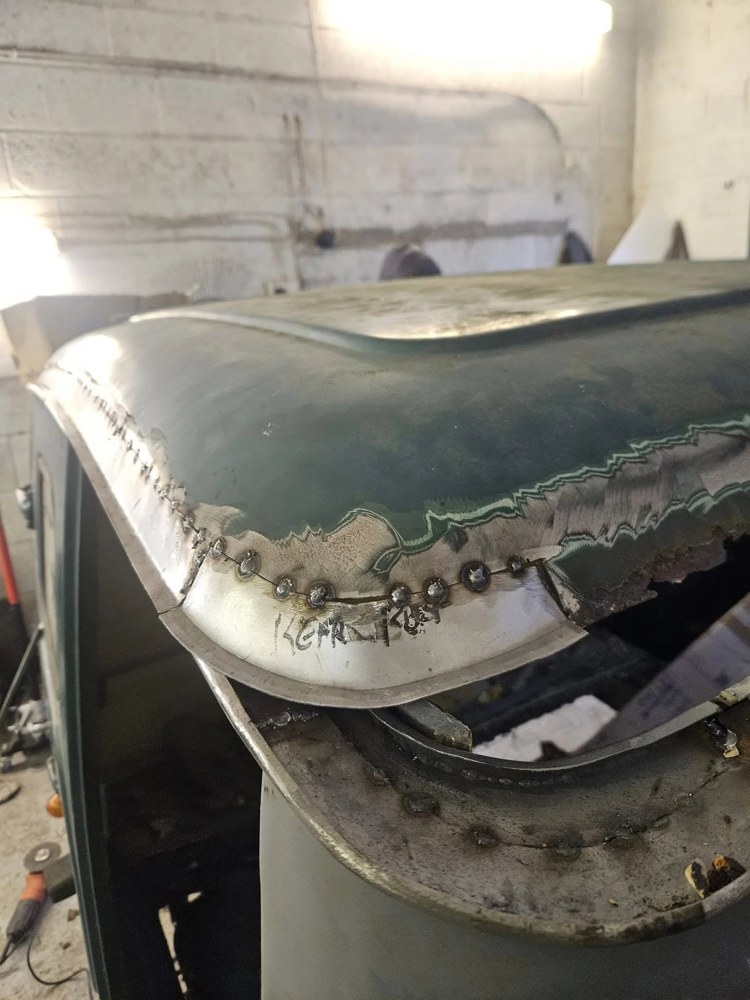 Close-up of a metallic object with a jagged edge, showing signs of welding and surface damage, all placed on a workbench in an industrial setting.