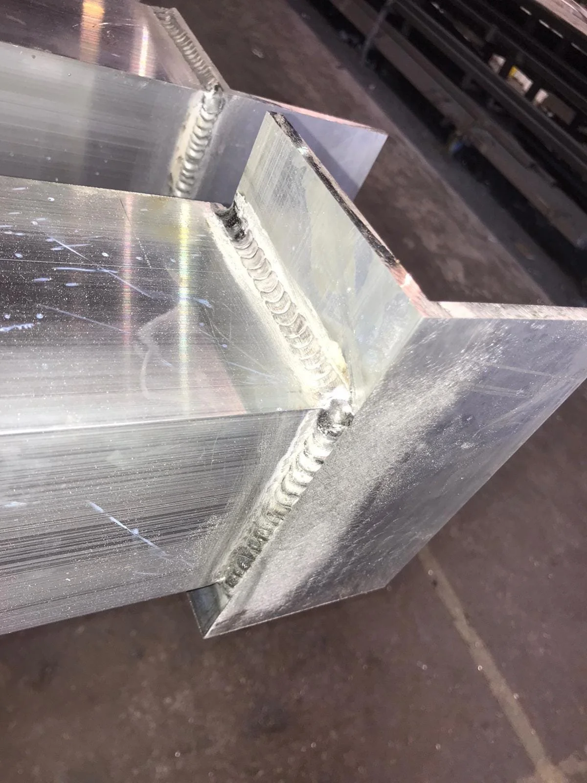 Close-up of a welded metal piece showing a clean, shiny weld bead along a corner joint with visible grinding marks.