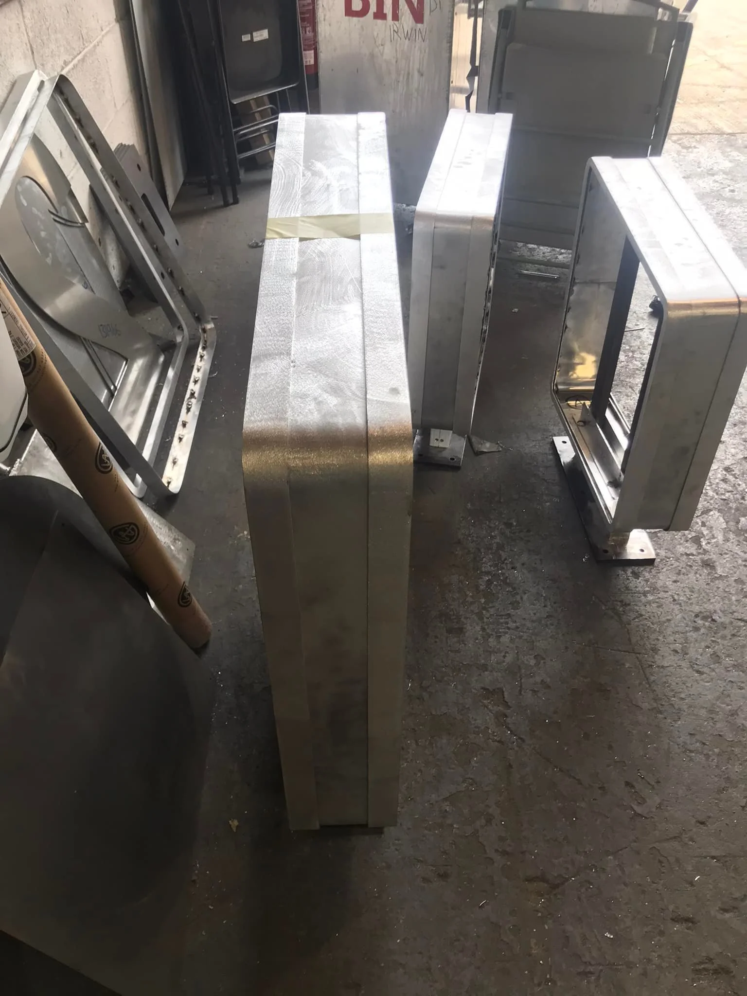 Stainless steel frames and panels for display or equipment, placed on a concrete floor in an industrial or warehouse setting.
