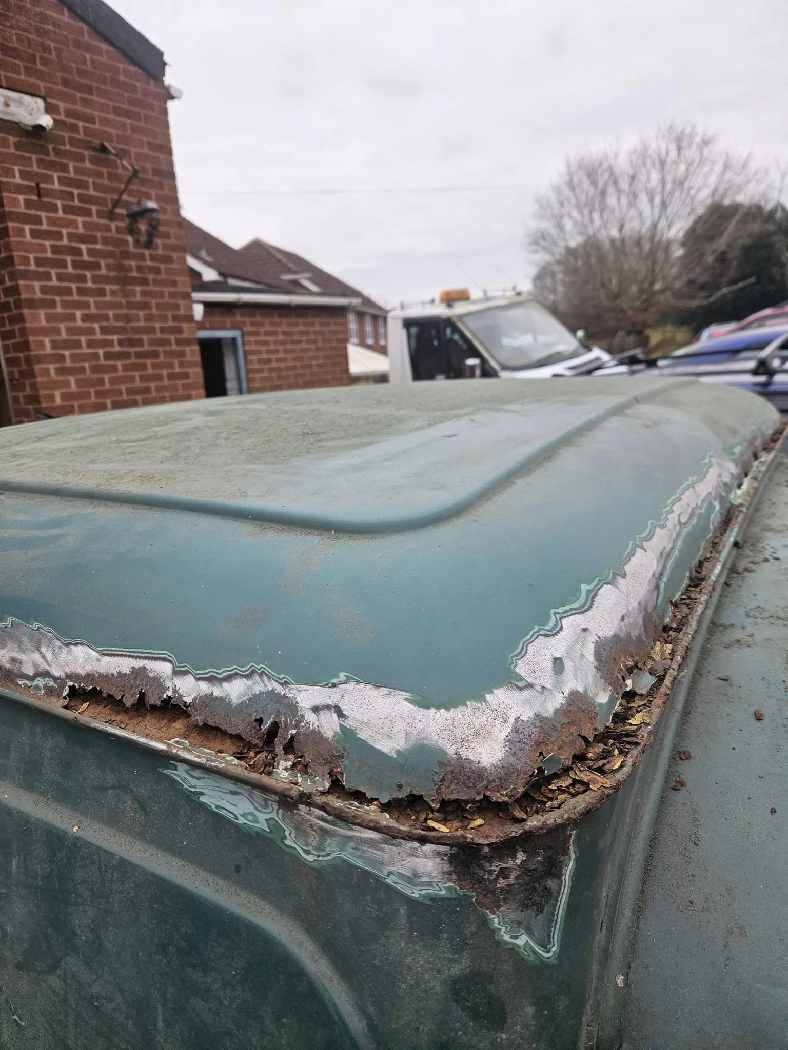 Close-up of a rusted, peeling, and corroded metal surface on the roof of a vehicle, with signs of deterioration and debris along the edges.