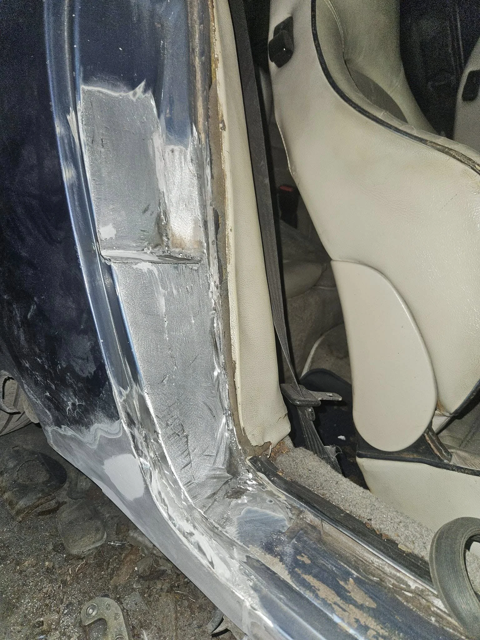Close-up of a car interior showing a damaged door frame with exposed metal and bodywork repair in progress.