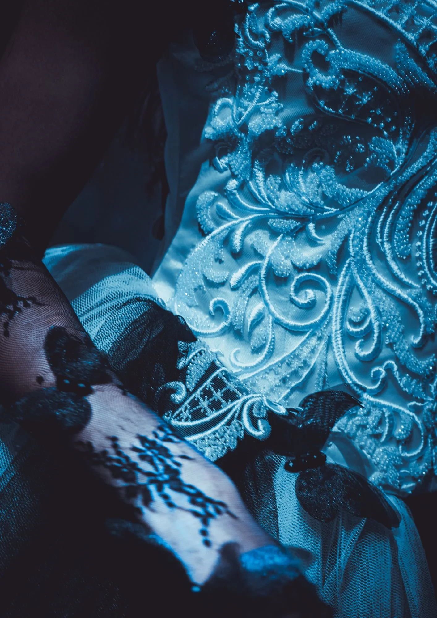 Close-up of a person wearing an intricate, beaded, and embroidered white dress with black lace sleeves.