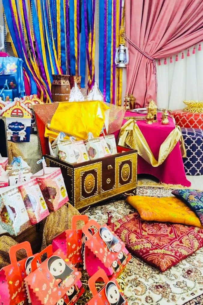 Colorful display of party decorations and supplies, including gift bags, pillows, and fabric drapes in pink, blue, yellow, and gold colors.