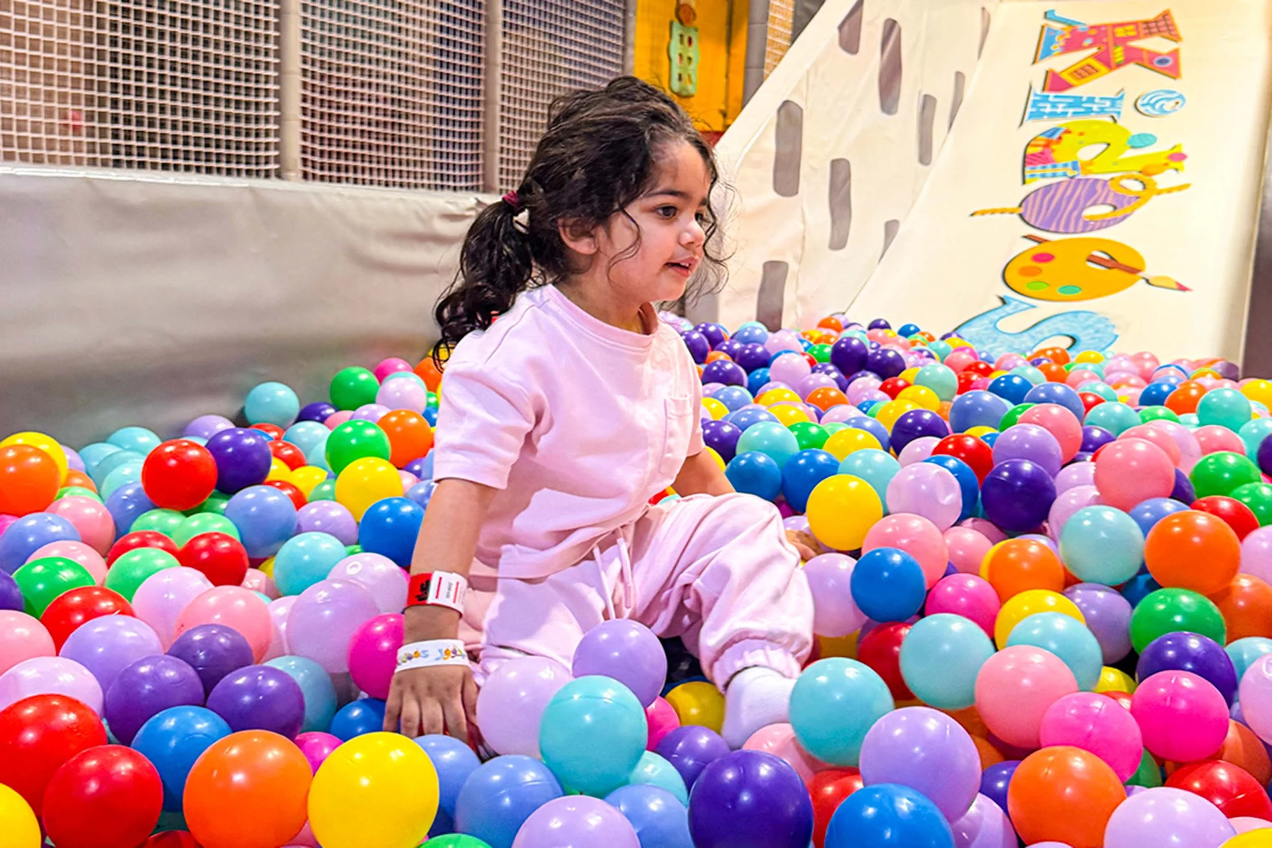 Young girl sitting in a colorful ball pit at an indoor play area.