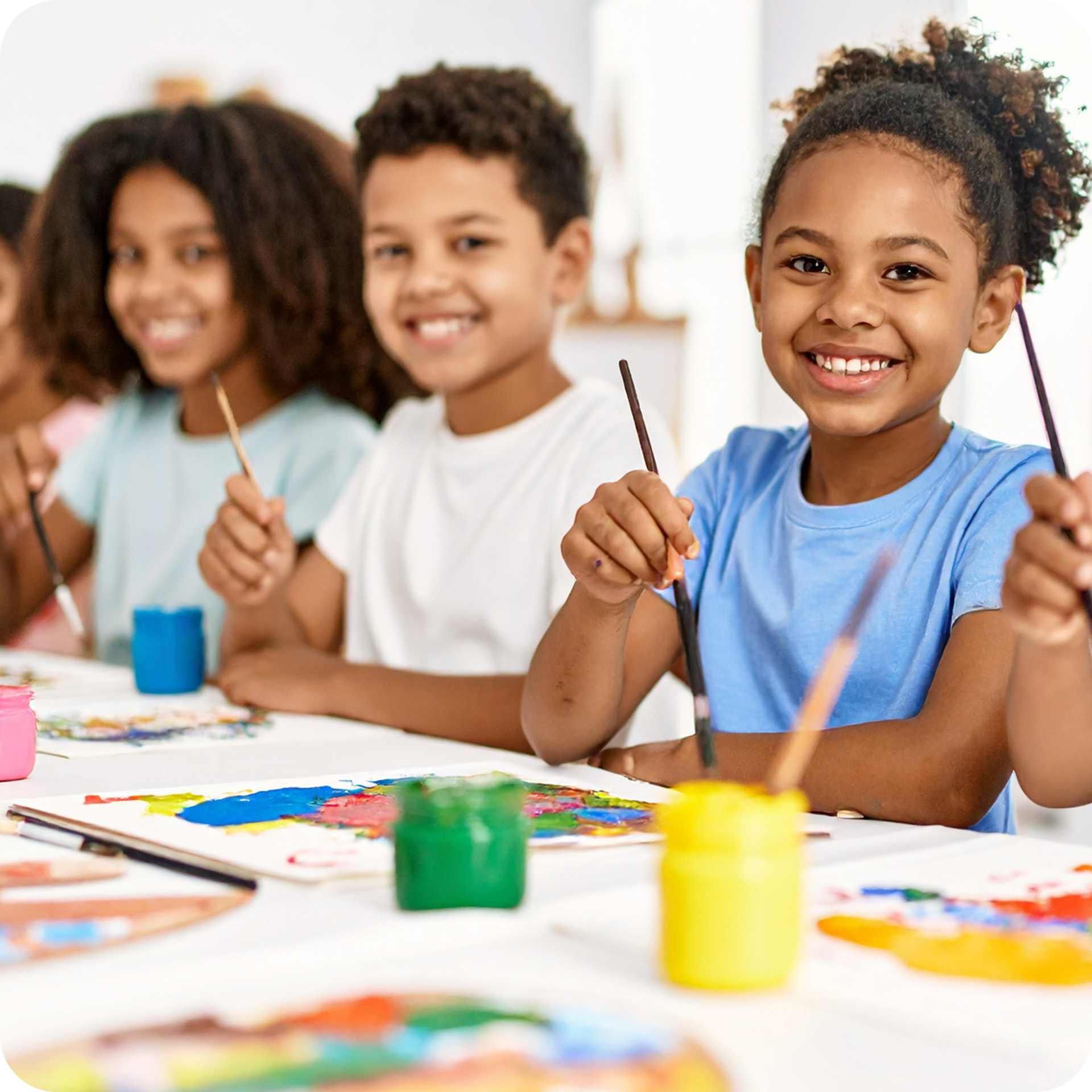 Children creating colorful paintings at a table in a classroom.