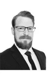 Portrait of a man with glasses, short hair, and a beard, wearing a suit and tie.